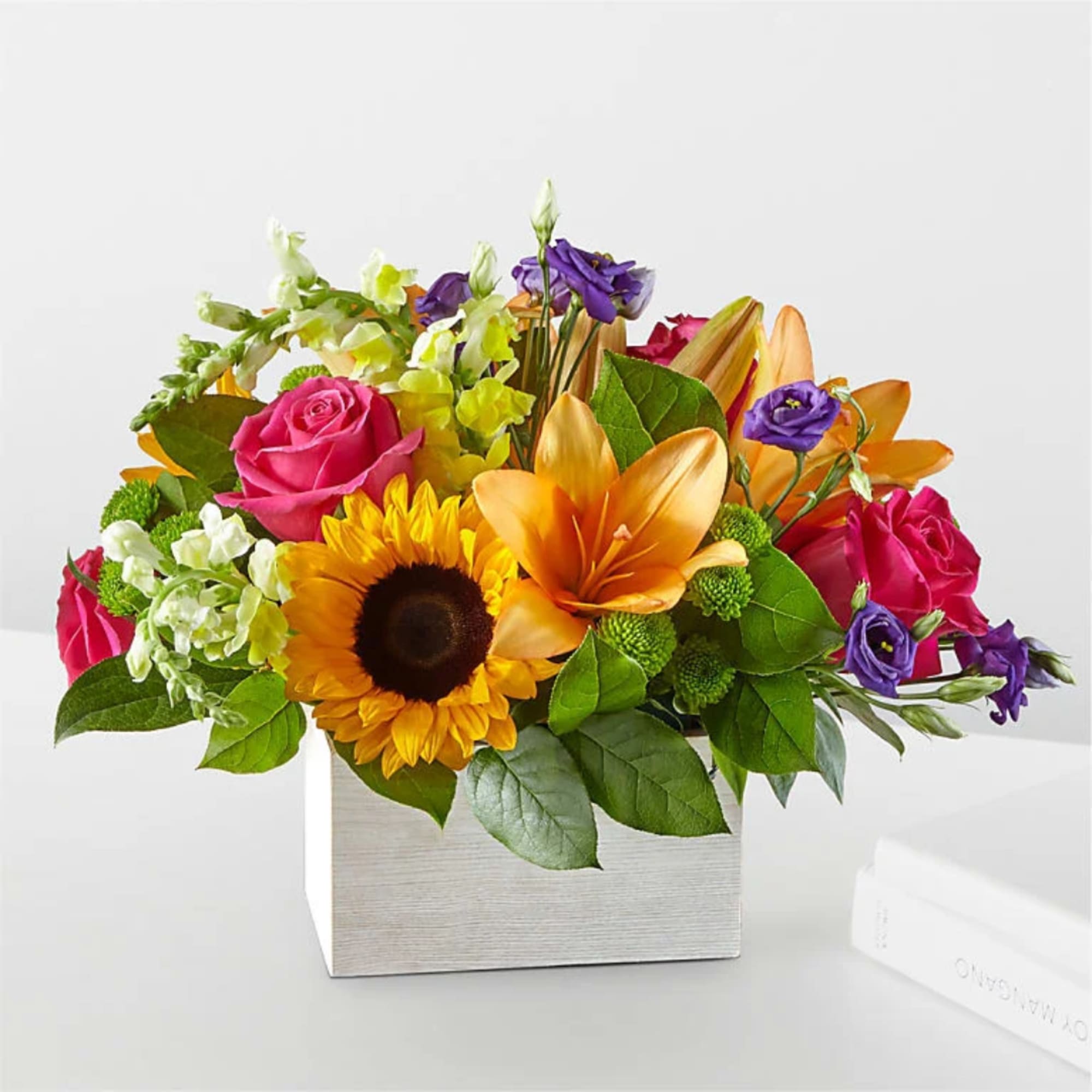 Mixed bouquet with sunflowers, roses, lilies, and purple blooms in a square box