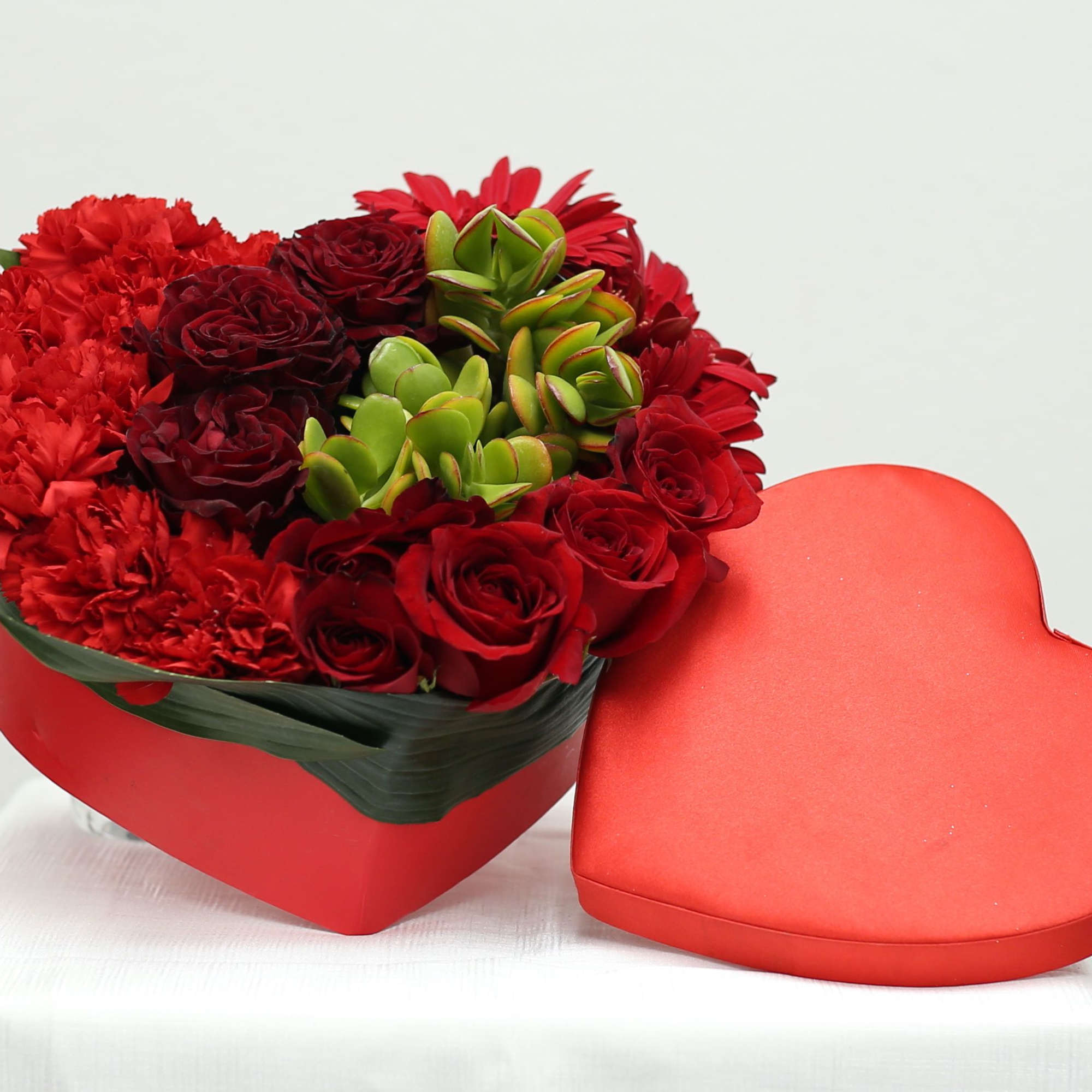 Heart-shaped box with red roses, carnations, and succulents