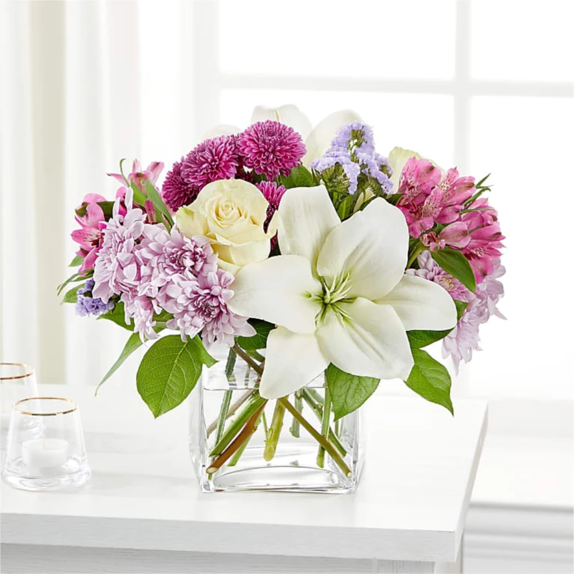 Mixed bouquet of white lilies, cream roses, and pink-purple flowers in a clear glass vase