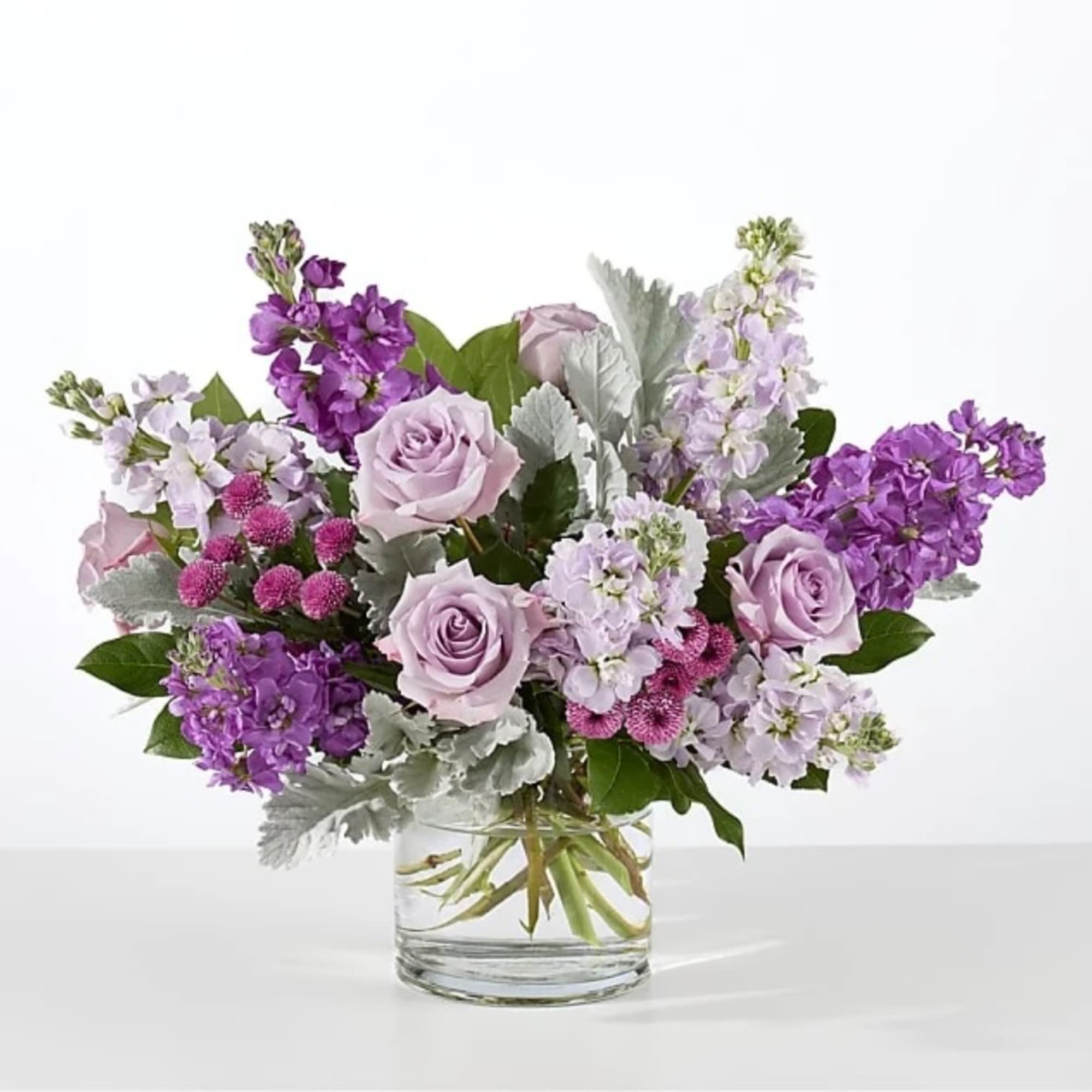 Lavender roses and purple flowers arranged in a clear glass vase