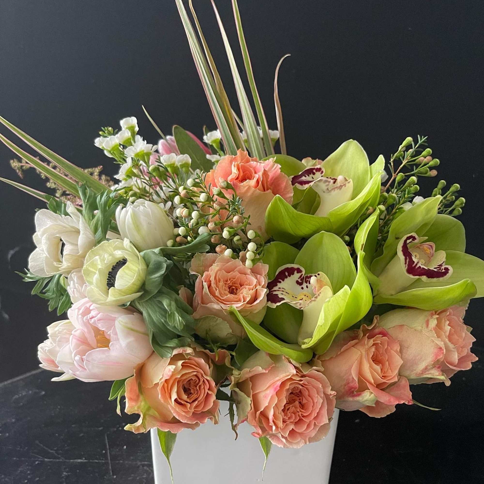 Mixed bouquet in a white square vase with peach roses and green orchids
