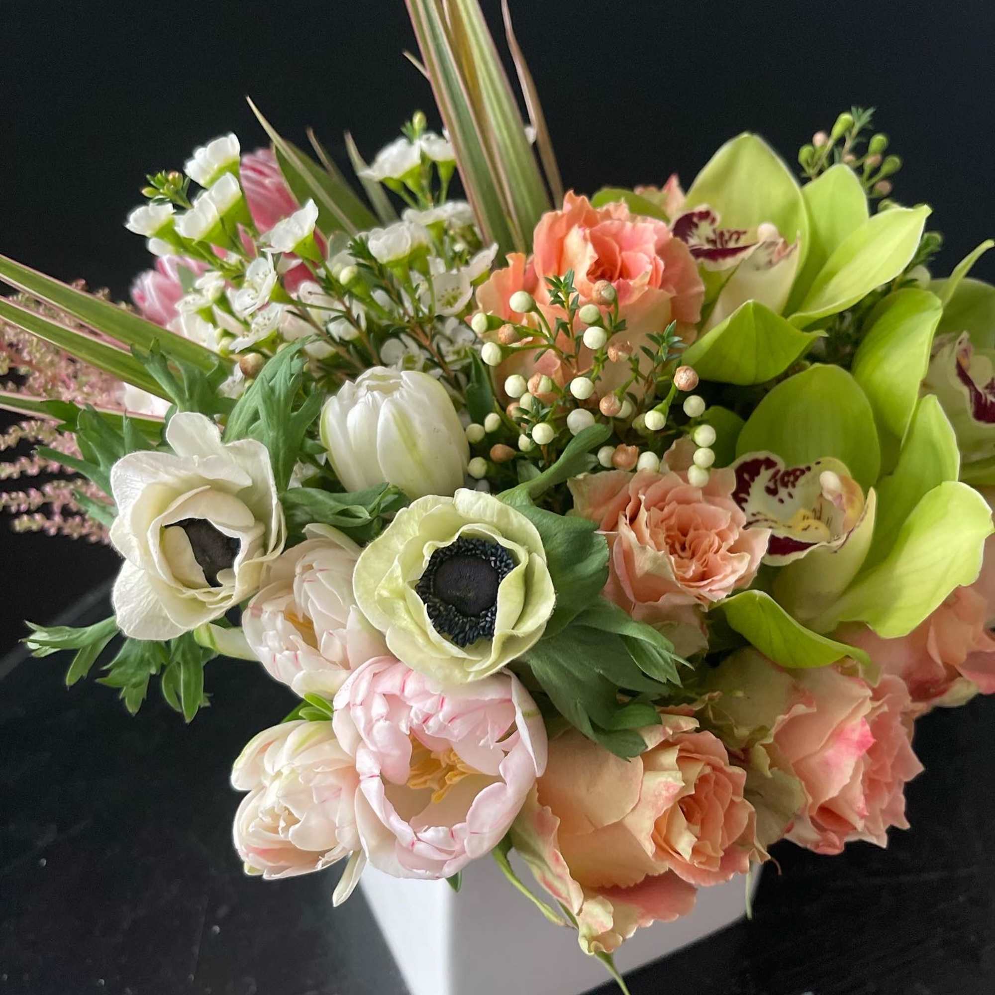 Mixed bouquet with pale pink, peach, white, and green flowers in a white vase