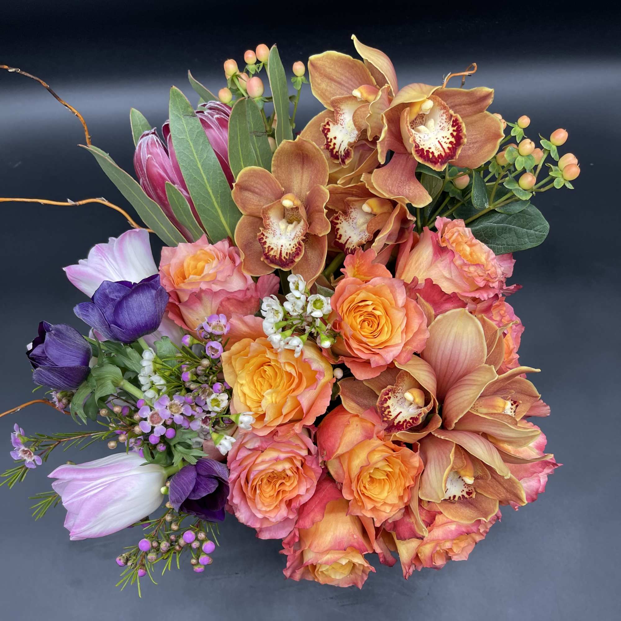 Mixed bouquet with orange roses, orchids, and purple blooms