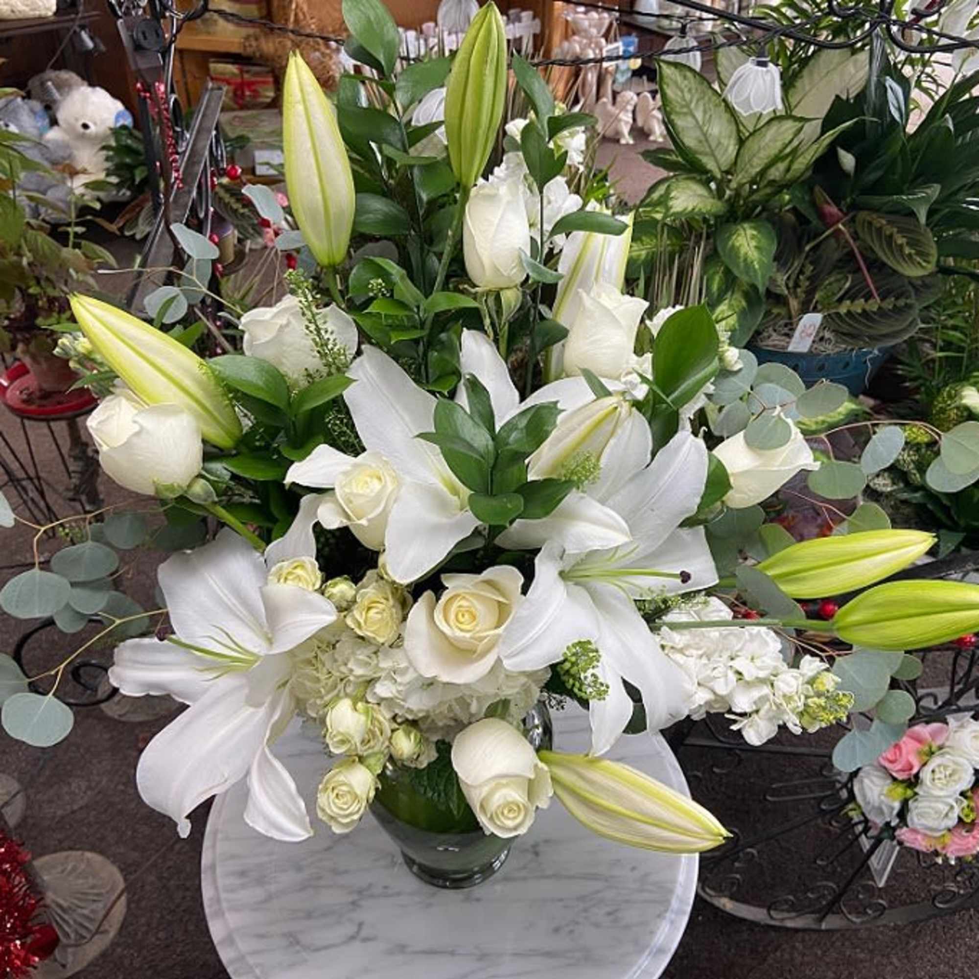Tall arrangement of white lilies and white roses in a clear glass vase on a round table