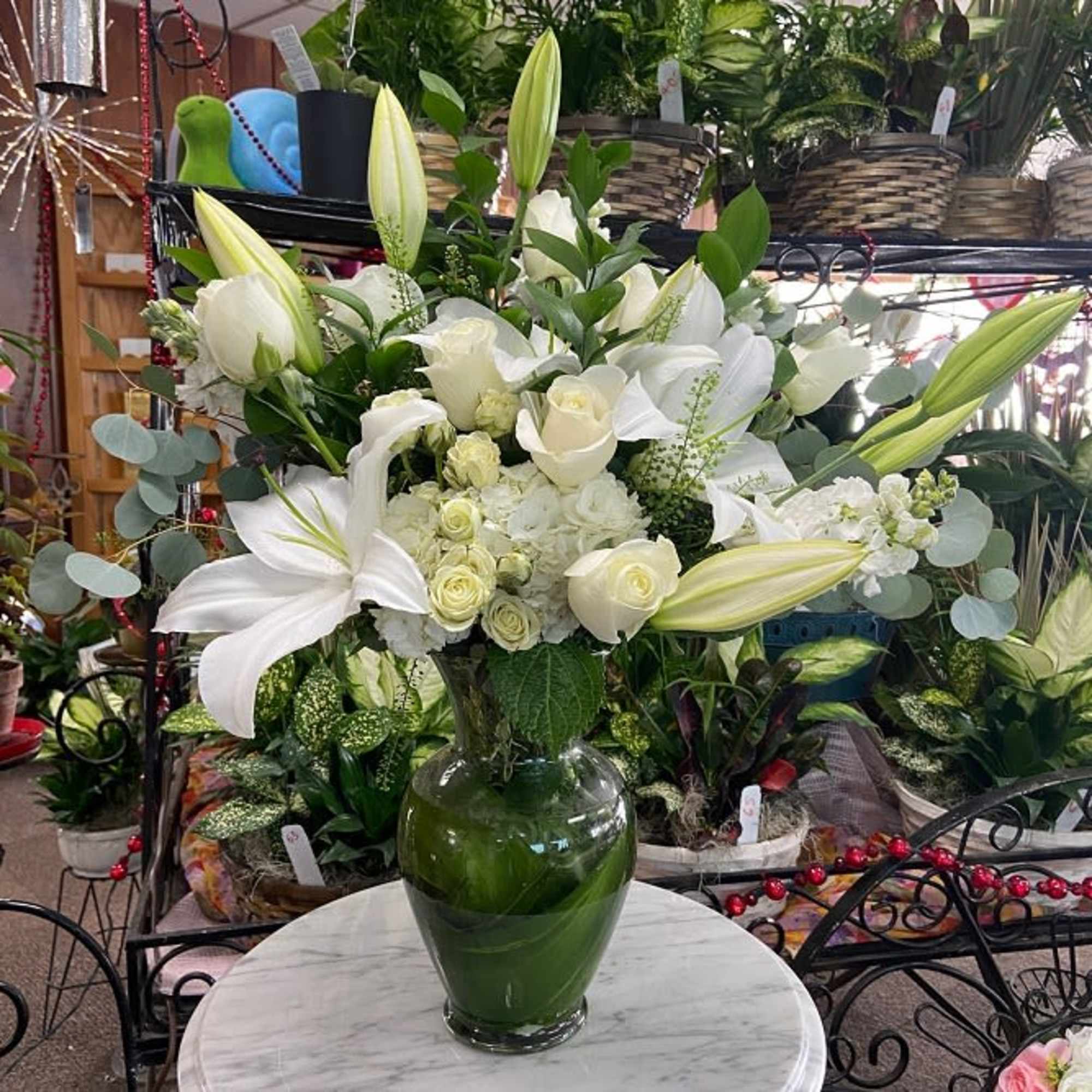 Tall arrangement of white lilies and roses in a clear glass vase on a table