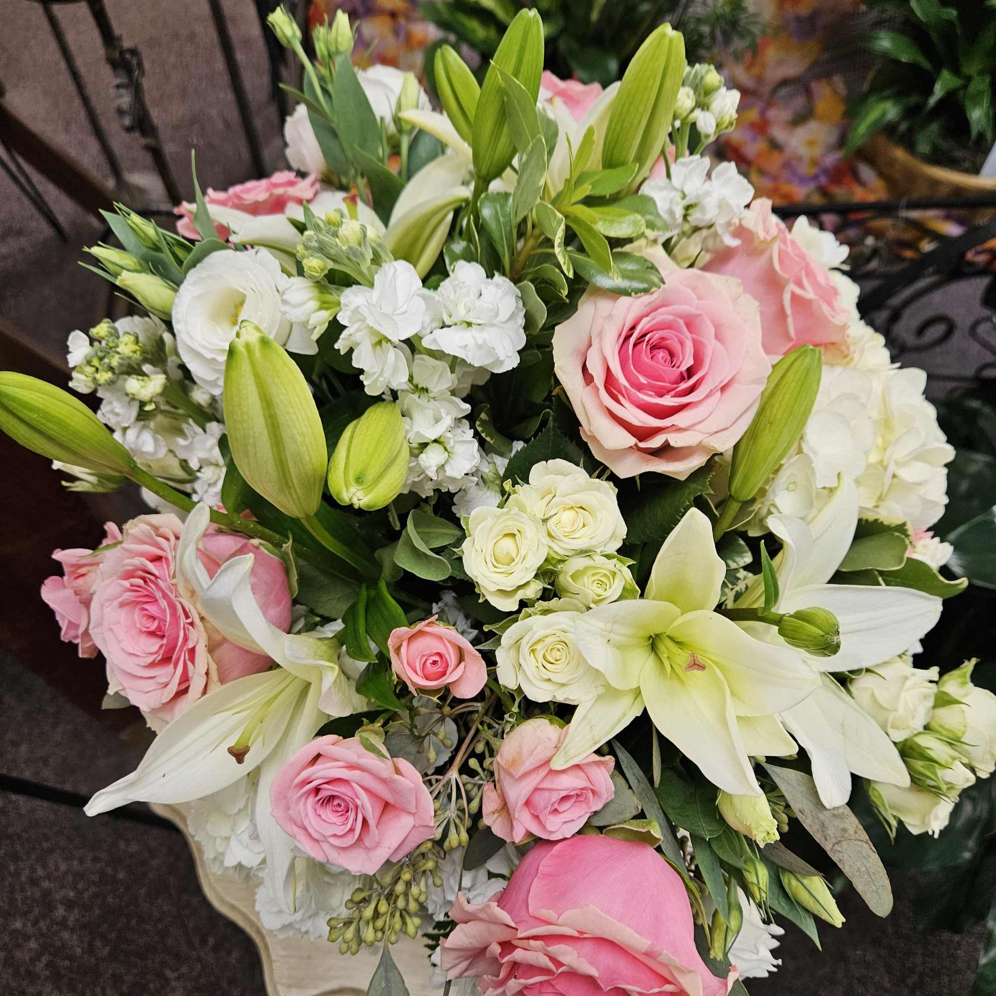 Large arrangement of pink roses and white lilies with small white blooms in a pedestal container