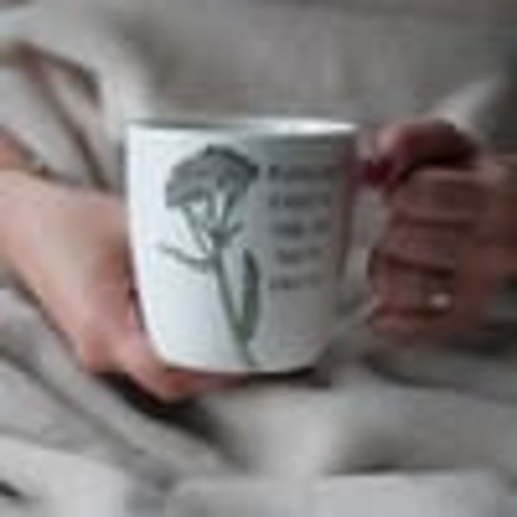 Person holding a white mug with a flower illustration