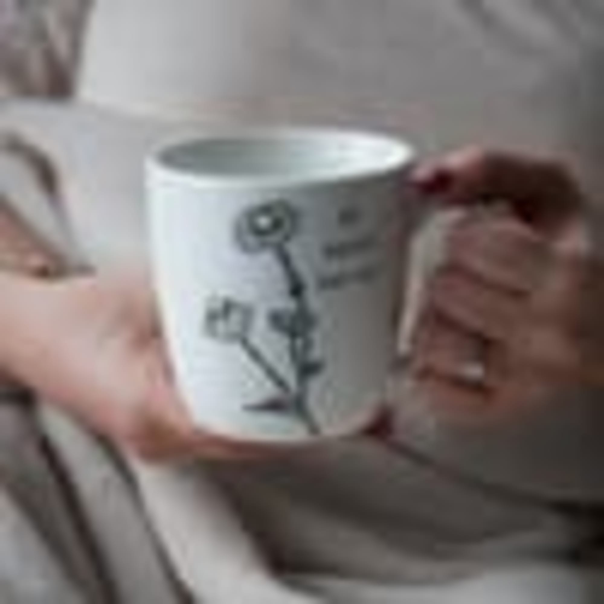 Hands holding a white mug with a floral line drawing
