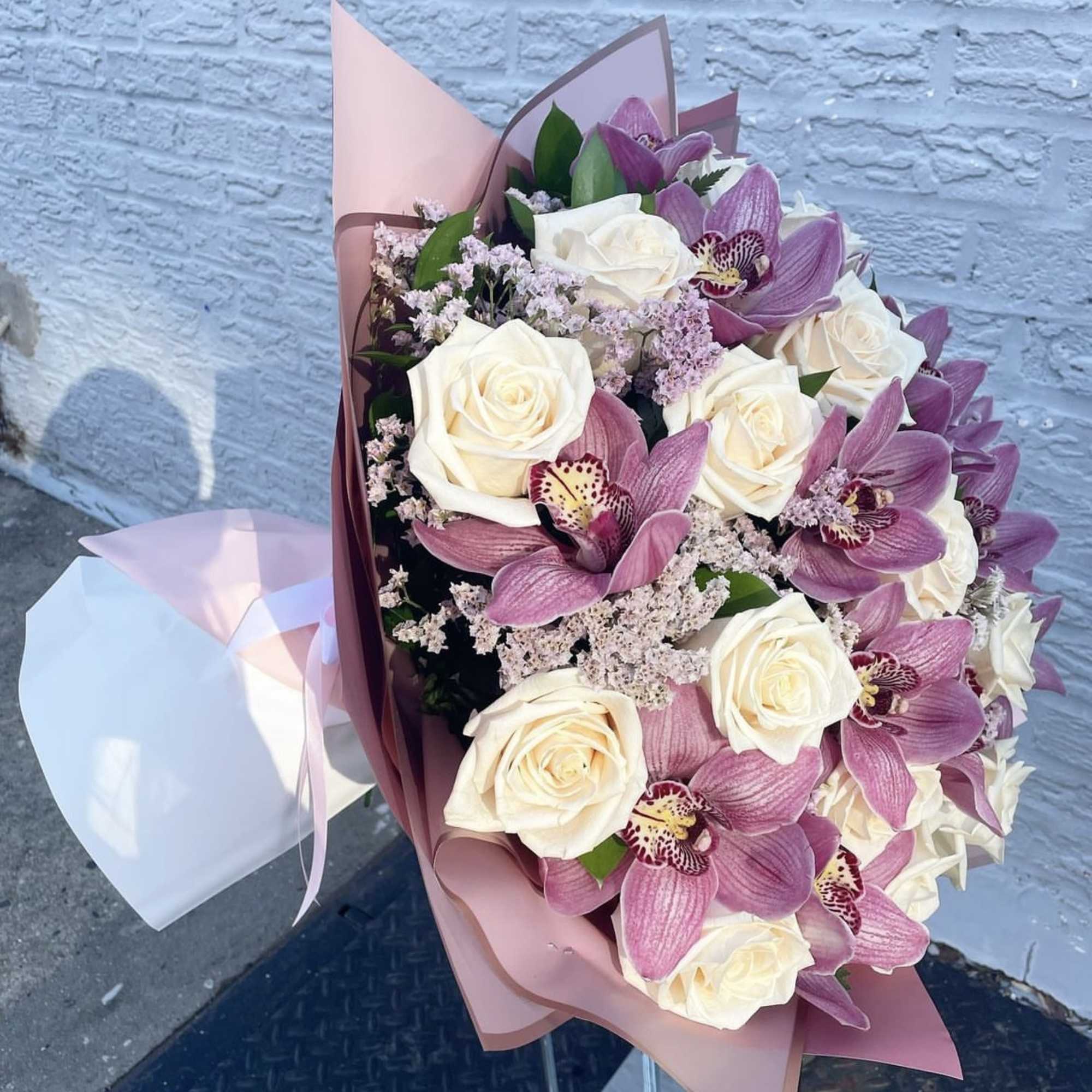 Bouquet of white roses and pink orchids wrapped in pink paper