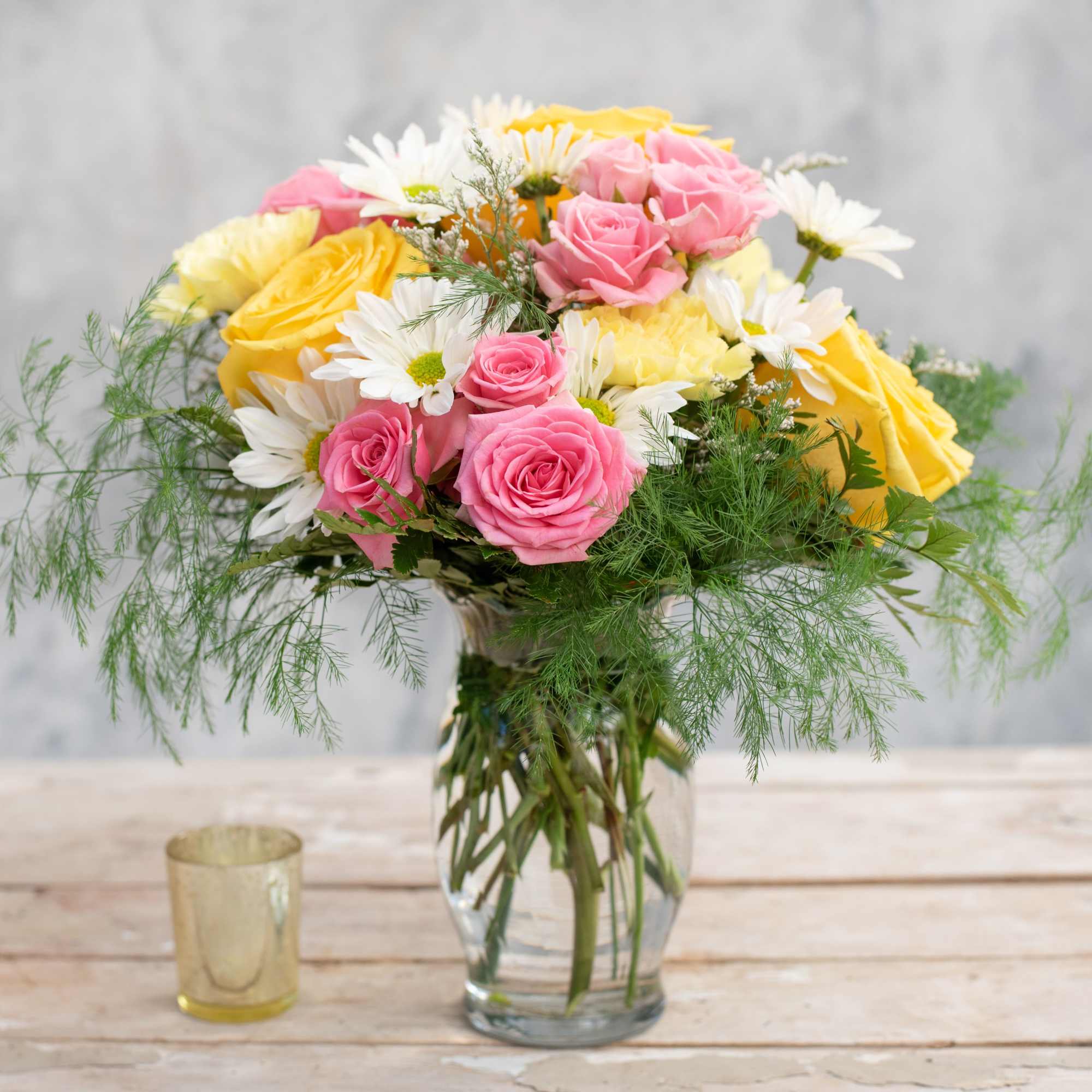 Pink and yellow roses with white daisies in a glass vase