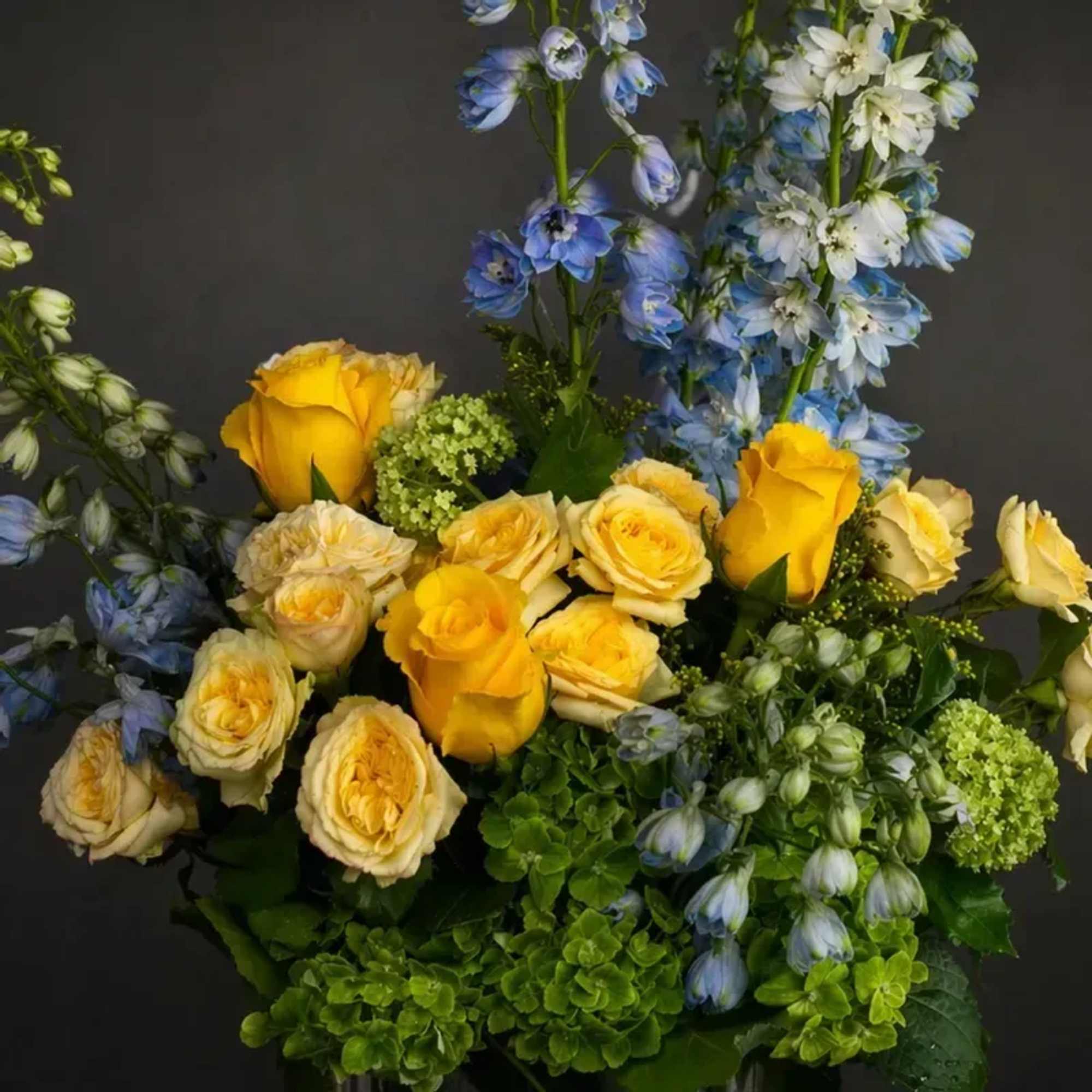 A fresh and airy arrangement featuring soft blue delphinium, sunny yellow and, photo 2 of 2