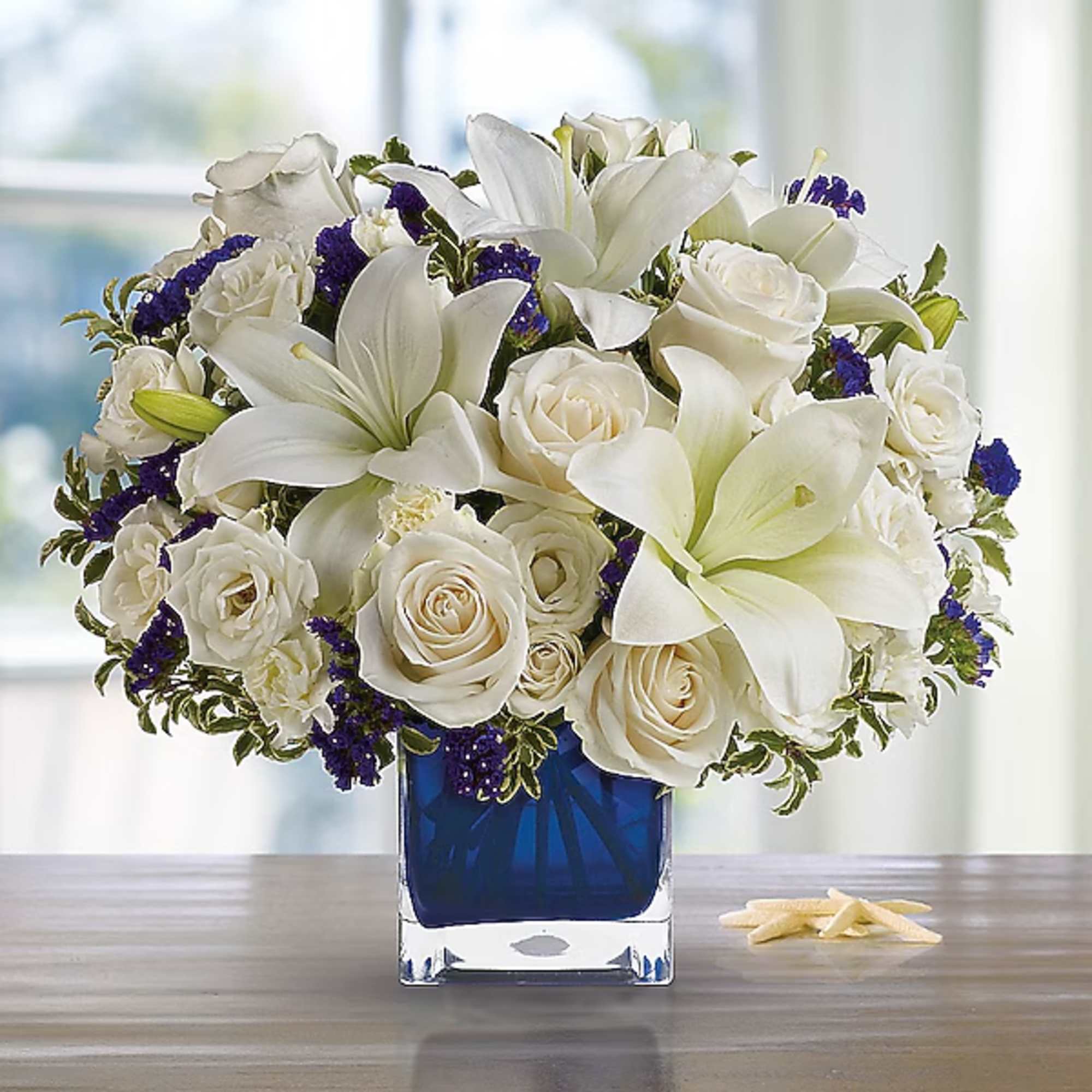 White roses and lilies arranged in a blue square vase