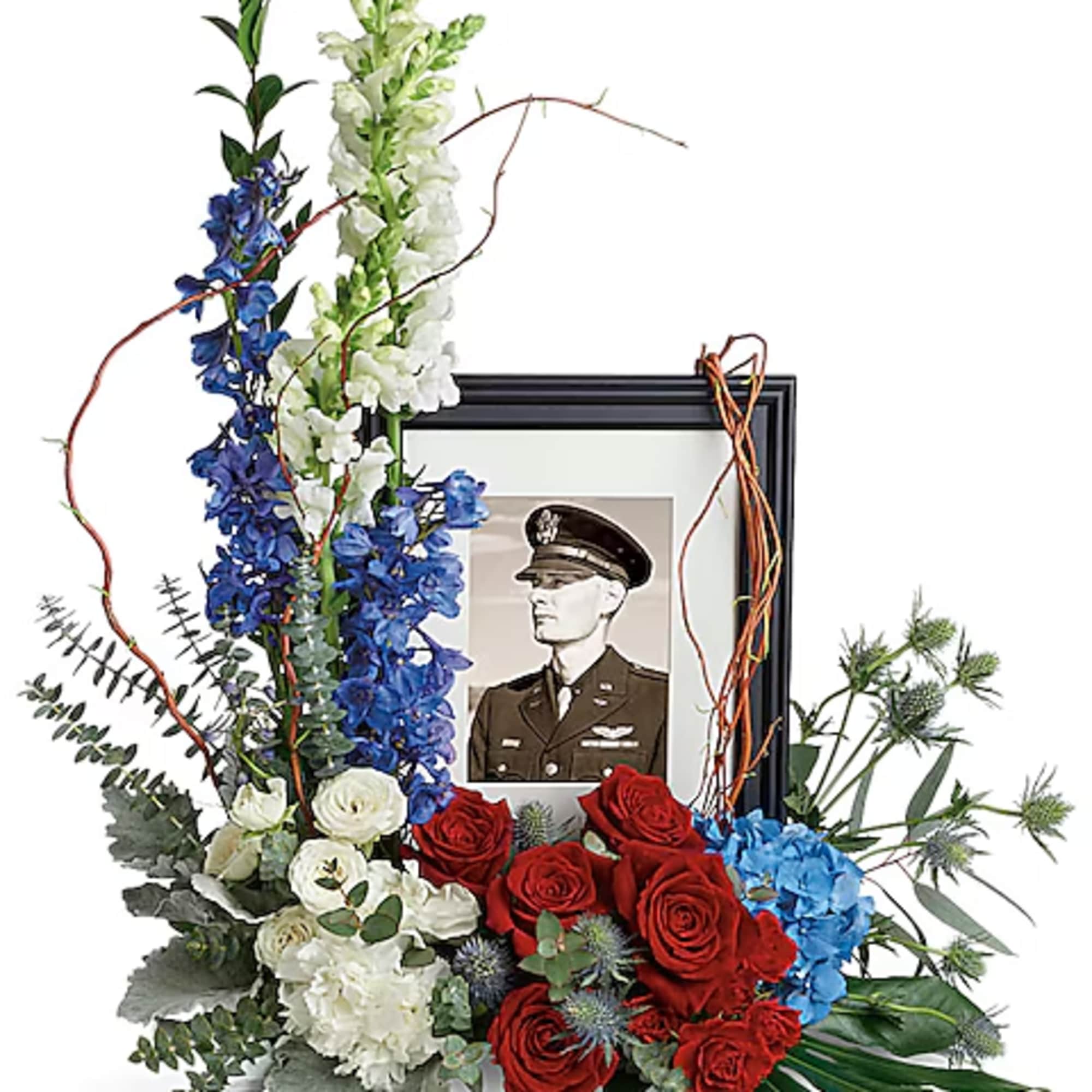 Floral tribute around a framed military portrait with red, white, and blue flowers