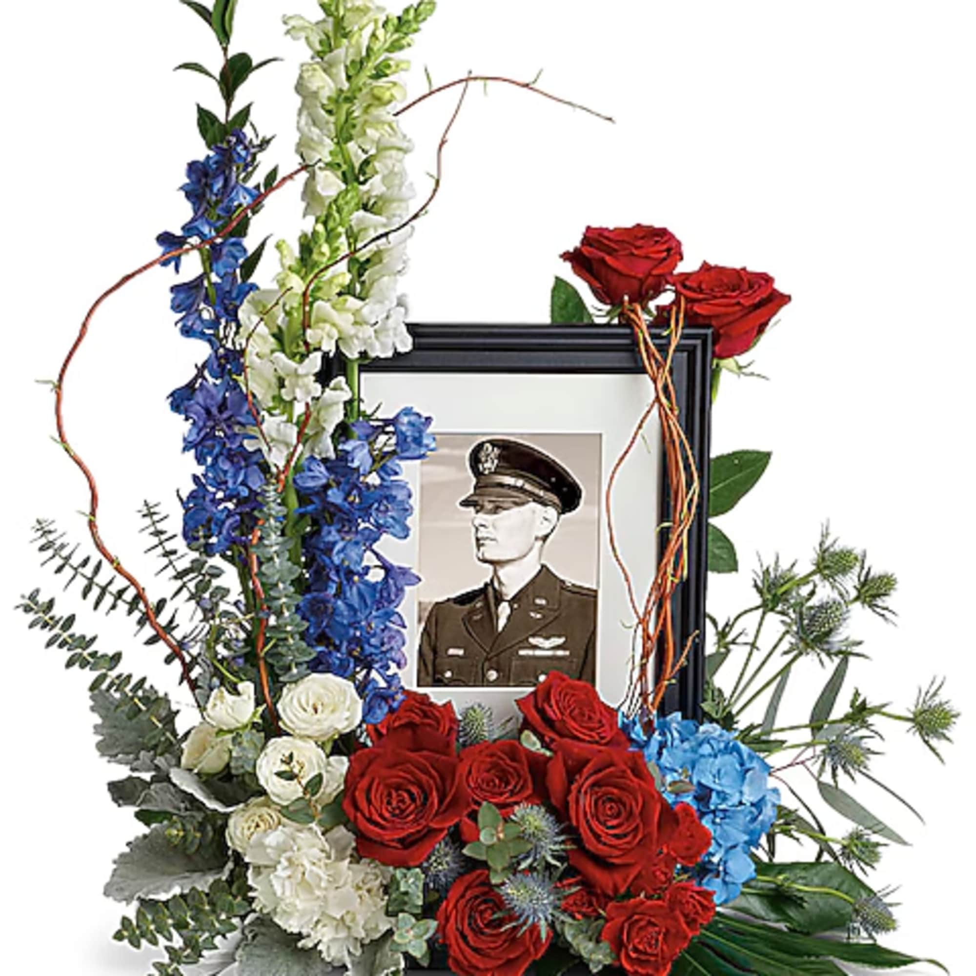 Floral tribute around a framed military portrait with red, white, and blue flowers