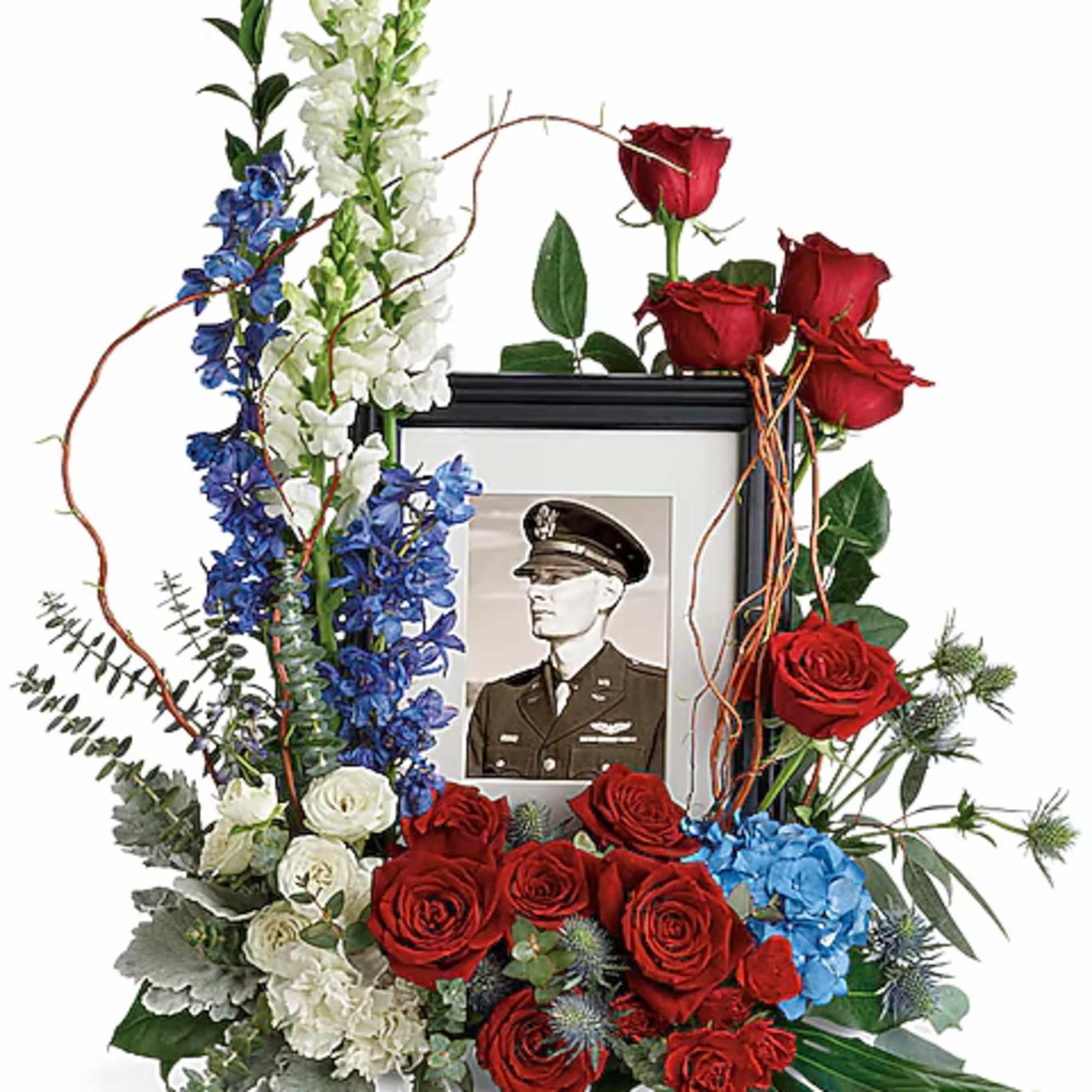 Floral tribute with red roses, blue and white flowers, and a framed portrait