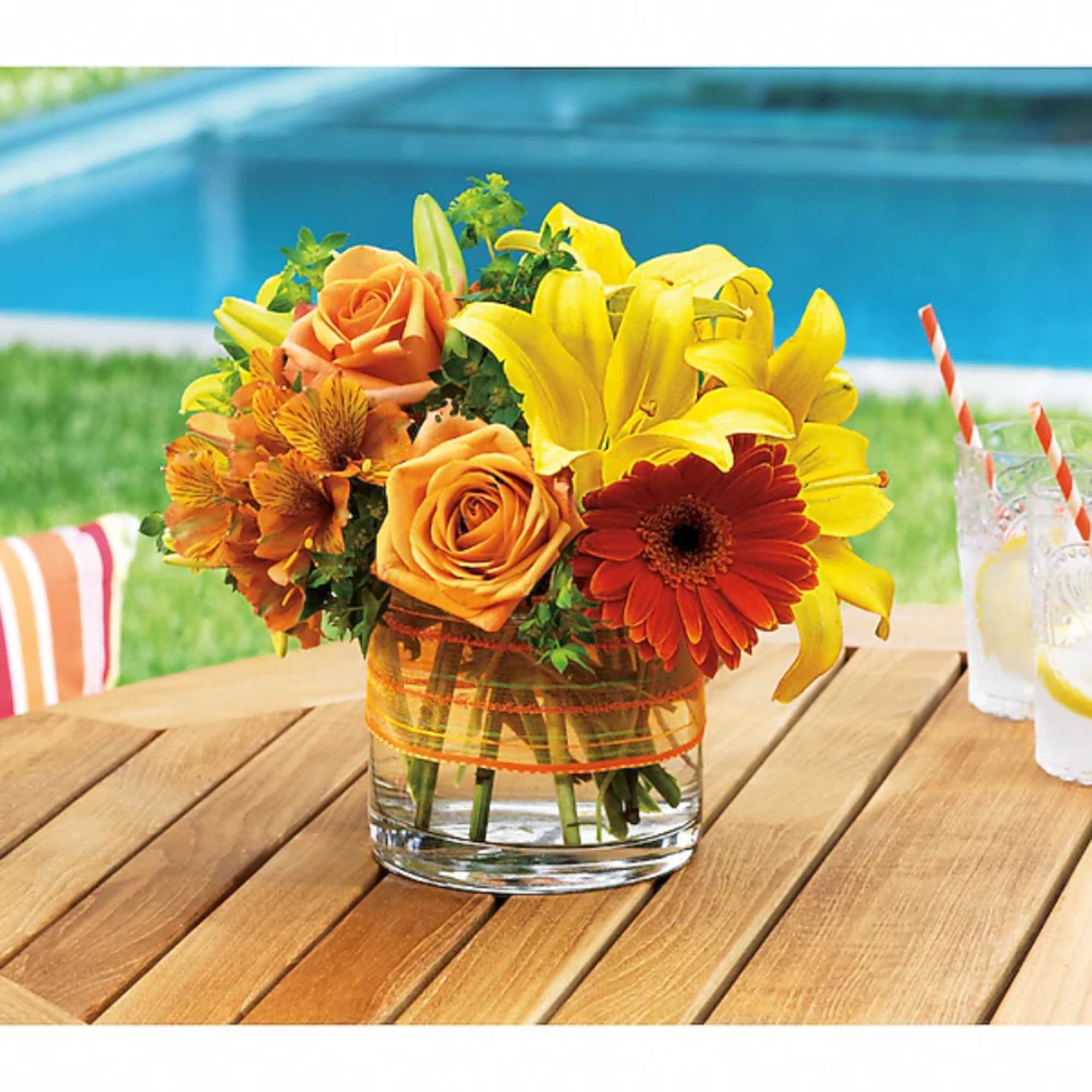Bouquet of yellow lilies, orange roses, and a red gerbera daisy in a glass vase