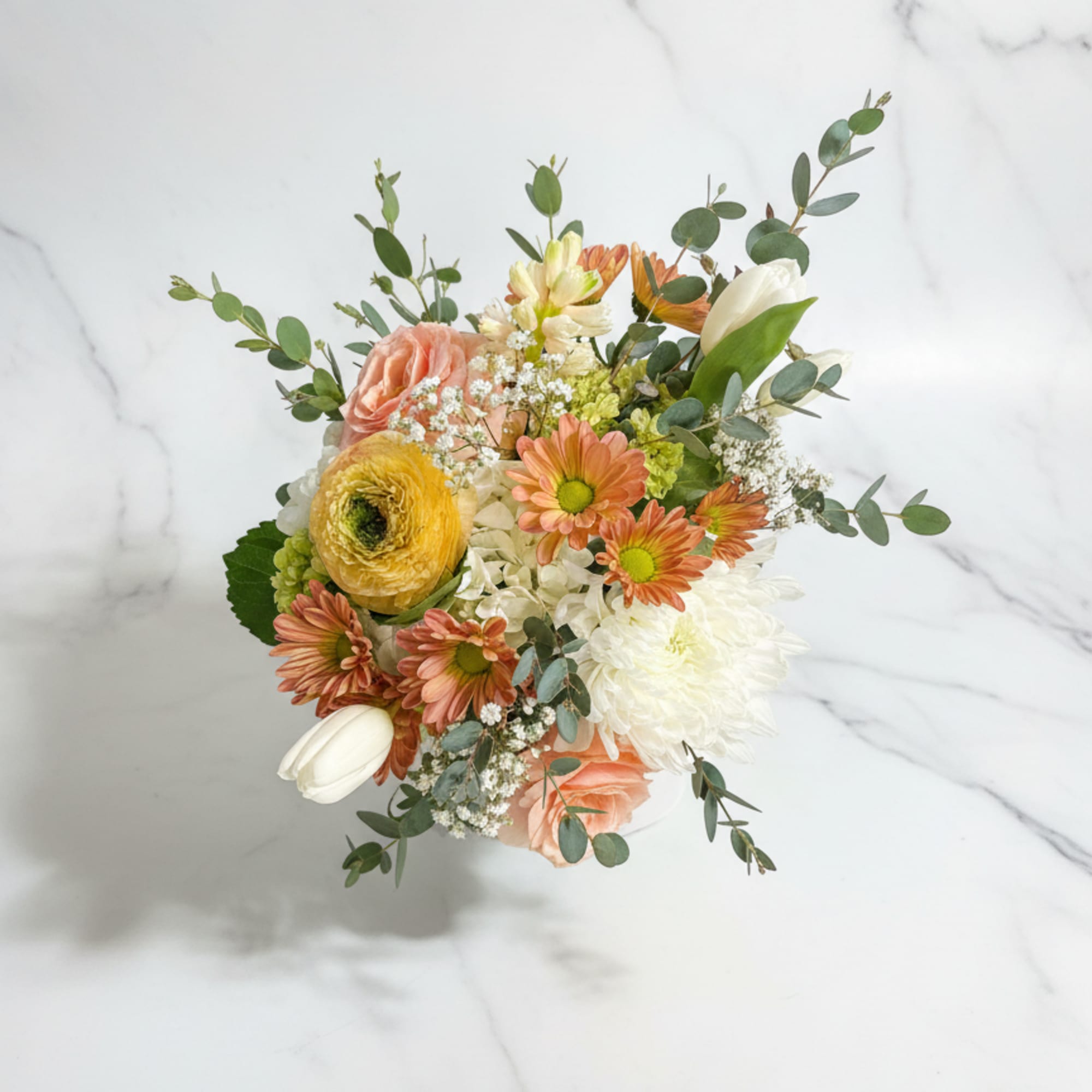 Compact arrangement of peach roses, daisies, tulips and white mums in a white vase