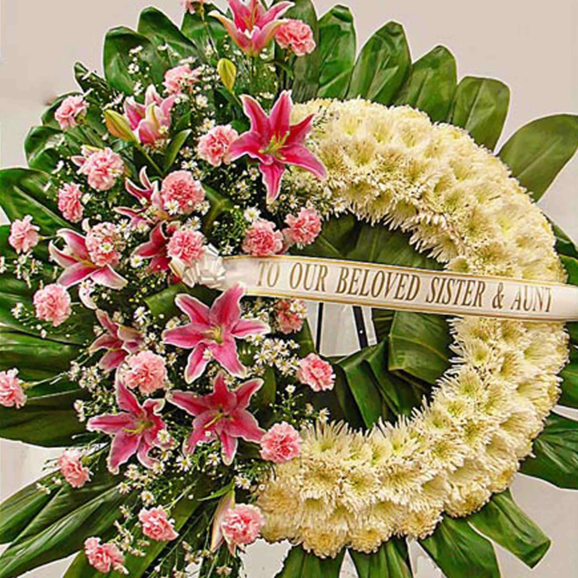 Large white wreath with pink lilies and carnations on a stand with a memorial ribbon