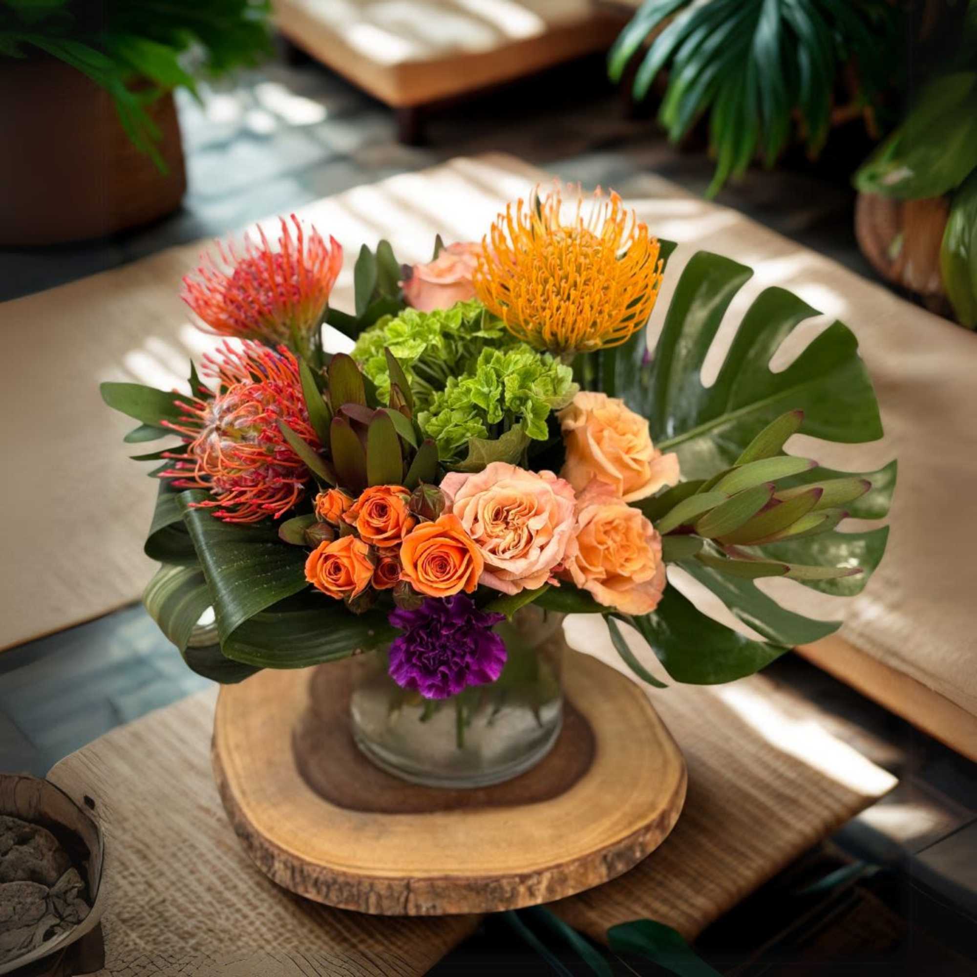 Tropical arrangement with orange protea, roses, and monstera leaves in a glass vase