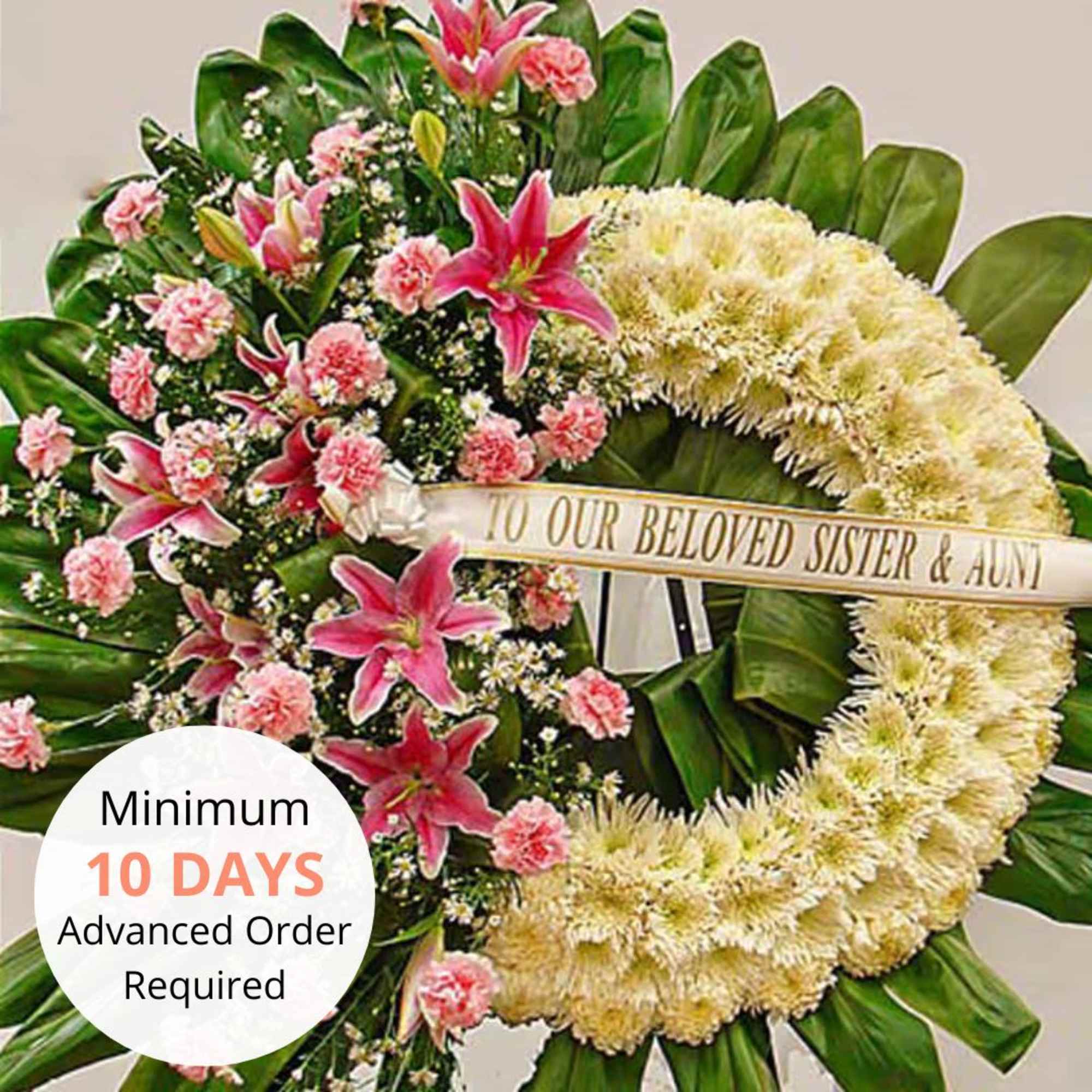 Standing funeral wreath with white mums, pink lilies, and carnations on large green leaves