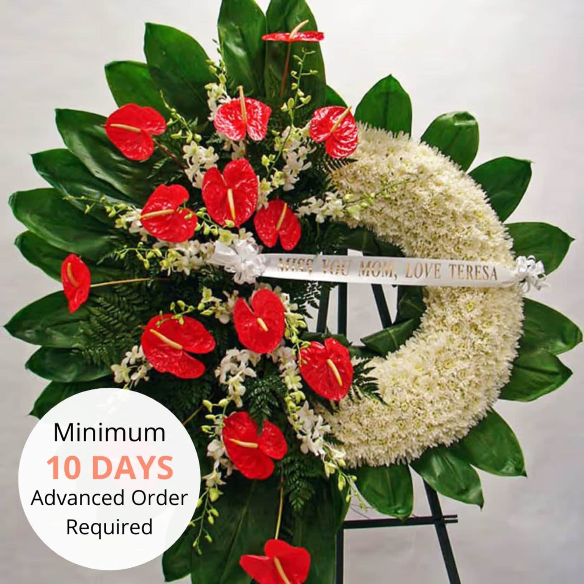 Tall standing crescent wreath with white flowers and red blooms on a green leaf backdrop.