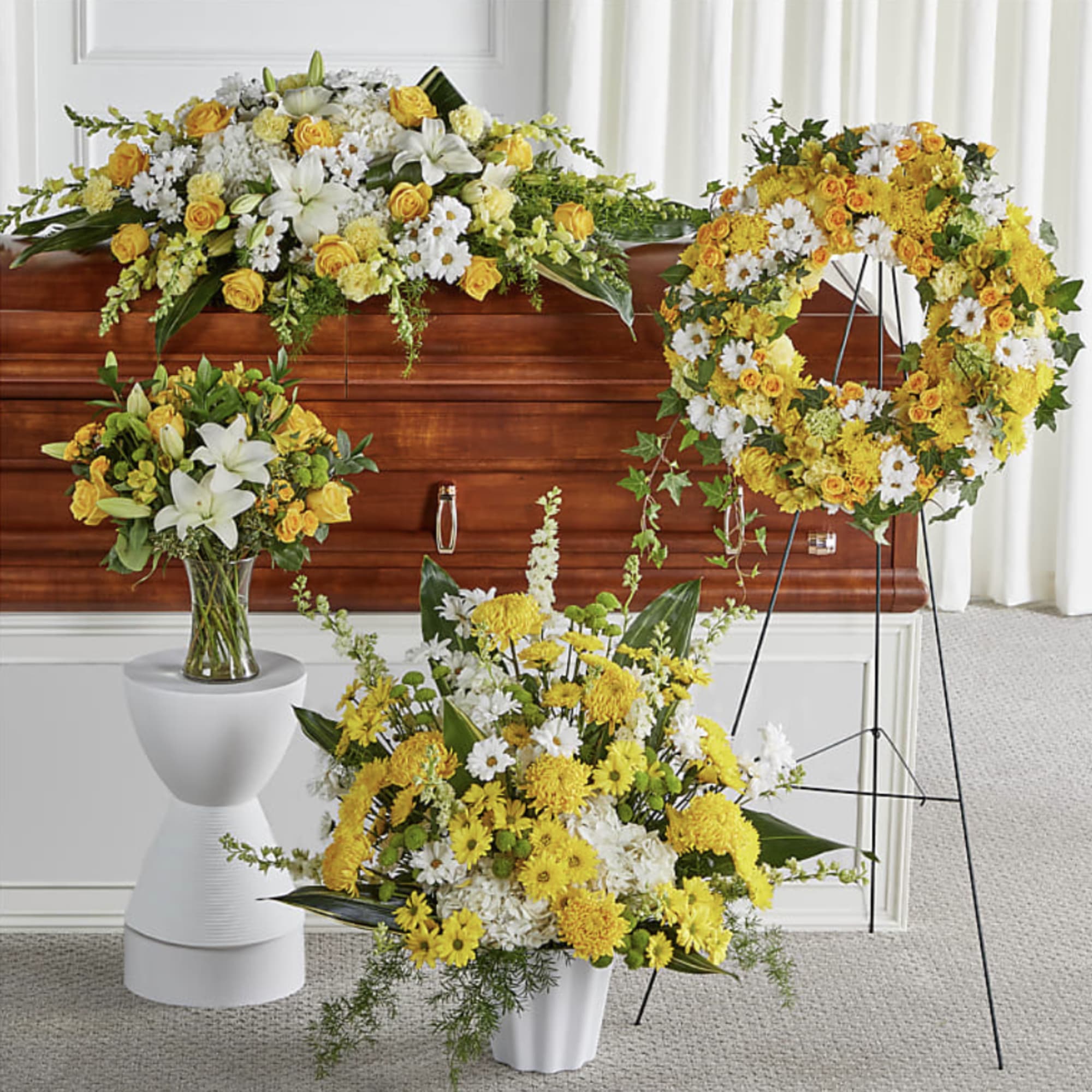 Yellow and white funeral floral set with casket spray, wreath, vase bouquet, and standing arrangement