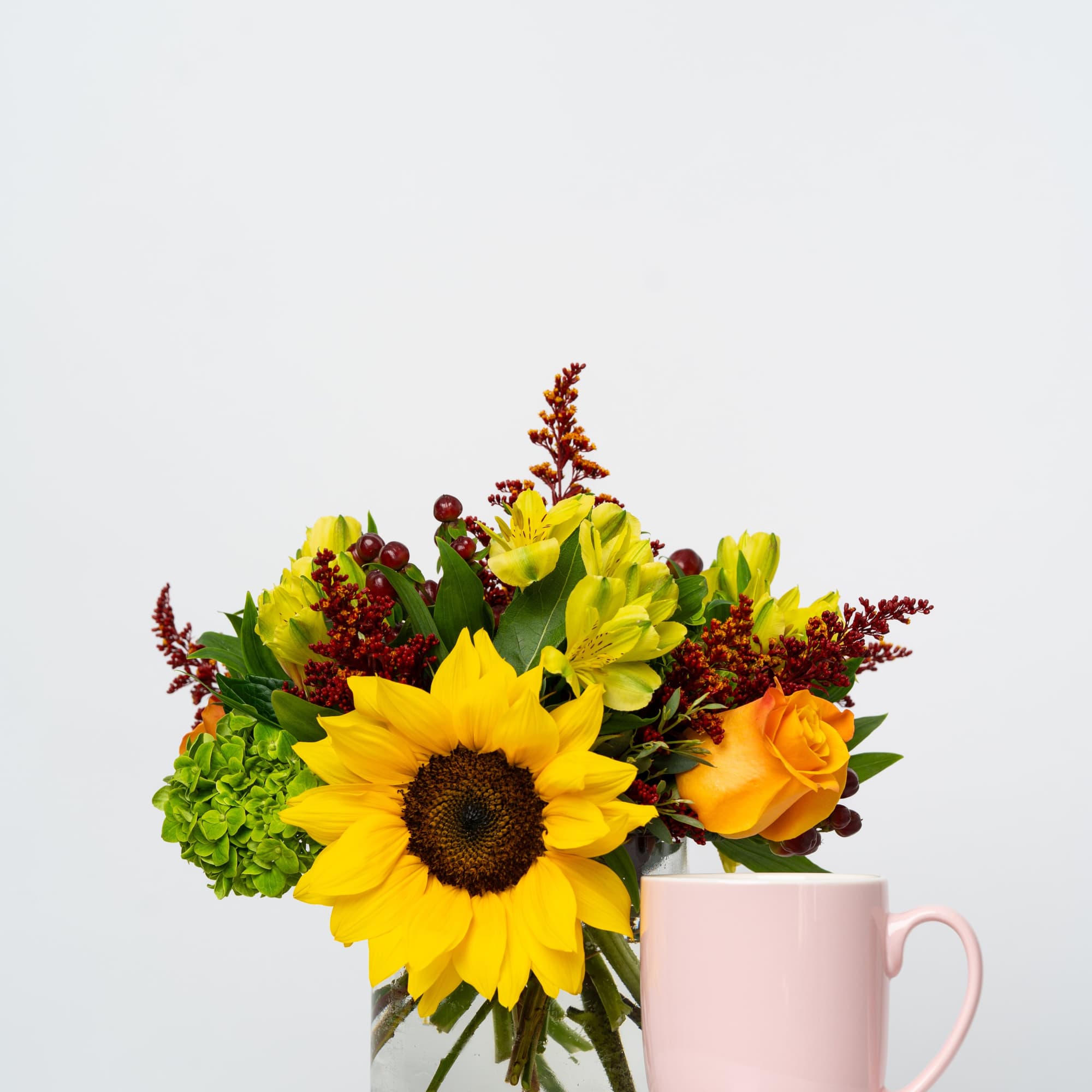 Sunflower and rose bouquet in a glass vase beside a pink mug