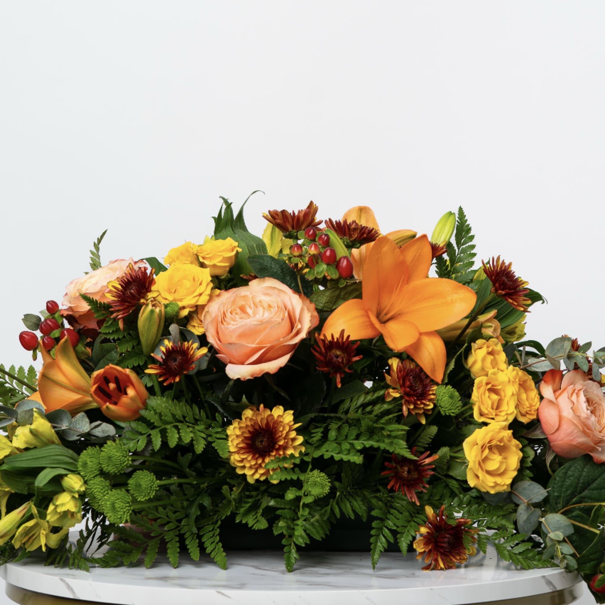 Low floral arrangement with orange lilies, peach roses, and yellow blooms