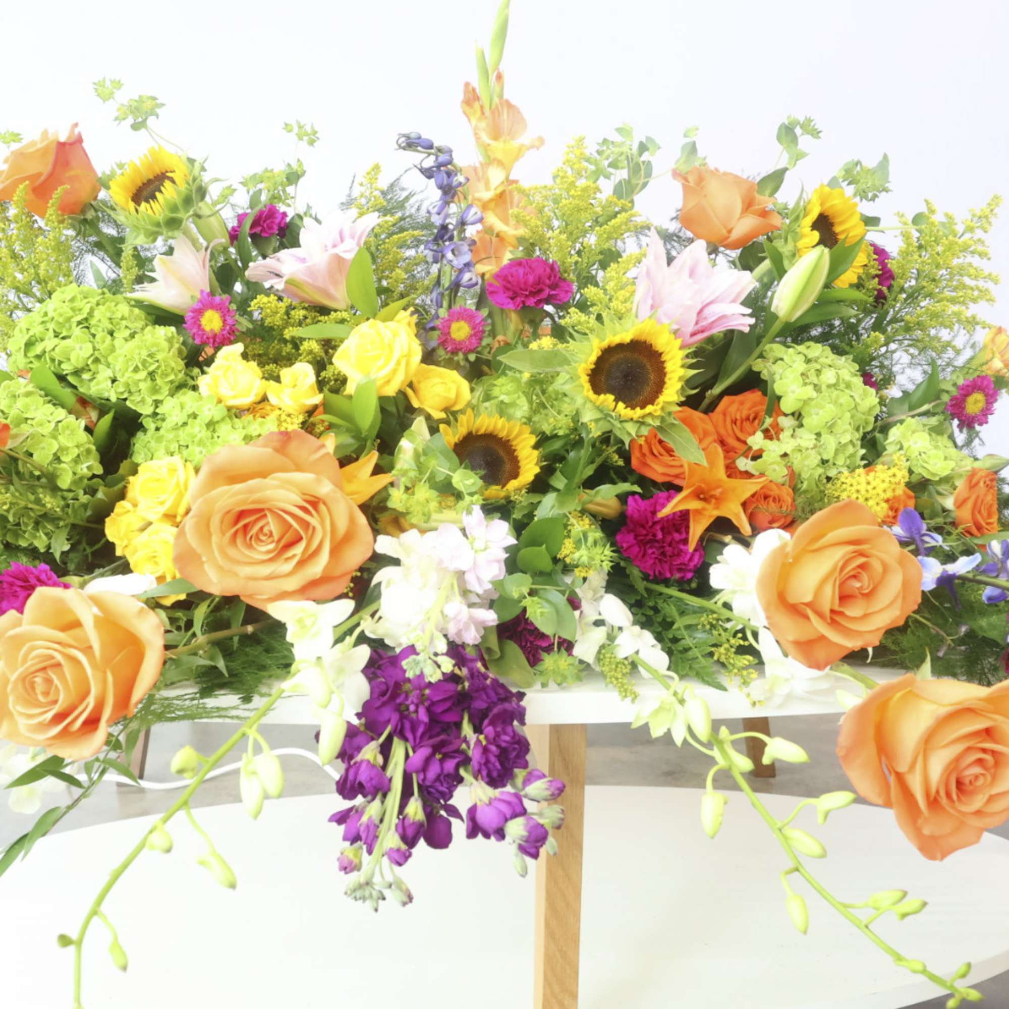 Large mixed floral arrangement with orange roses, sunflowers, and lilies