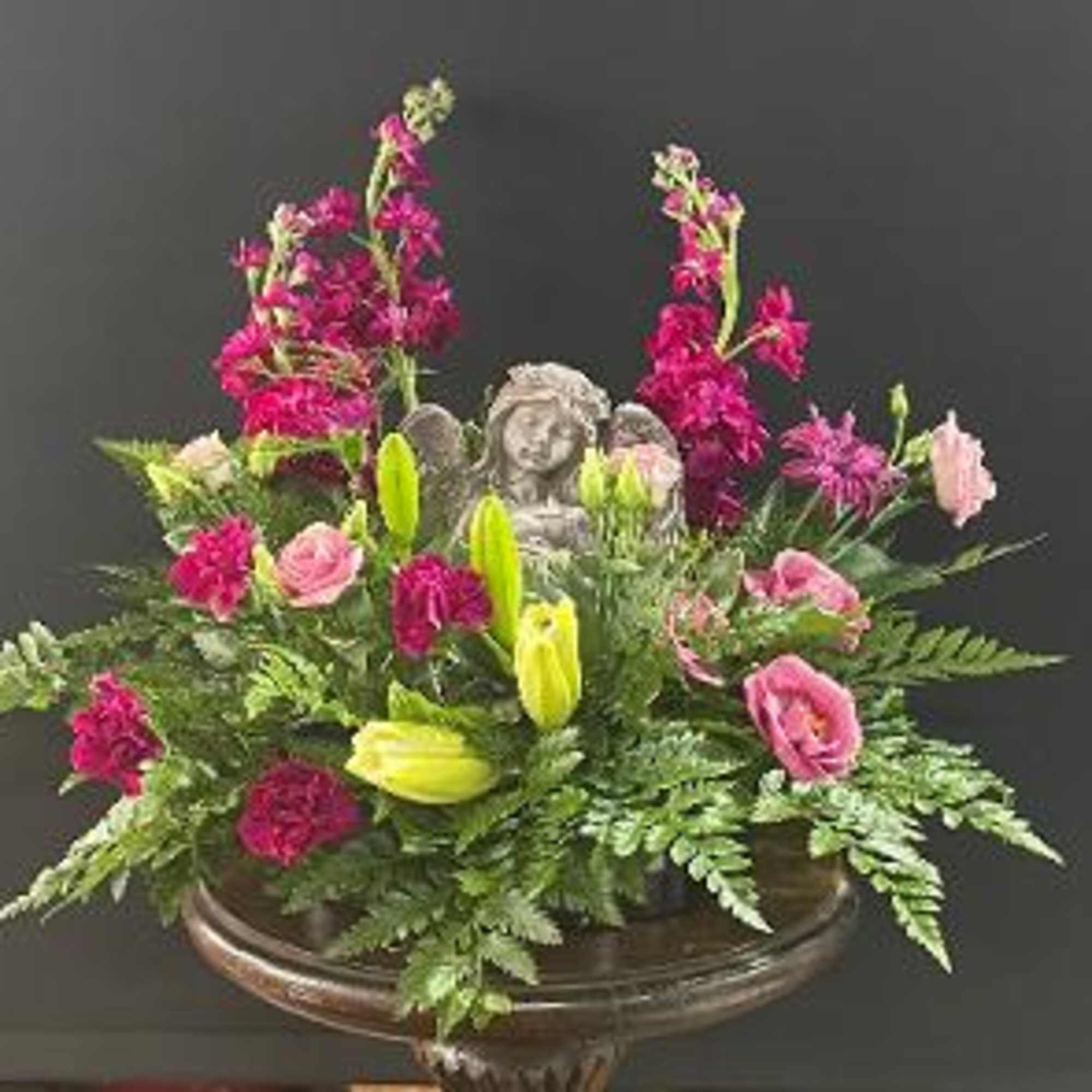 Pink and yellow floral arrangement with a small angel statue in a vase