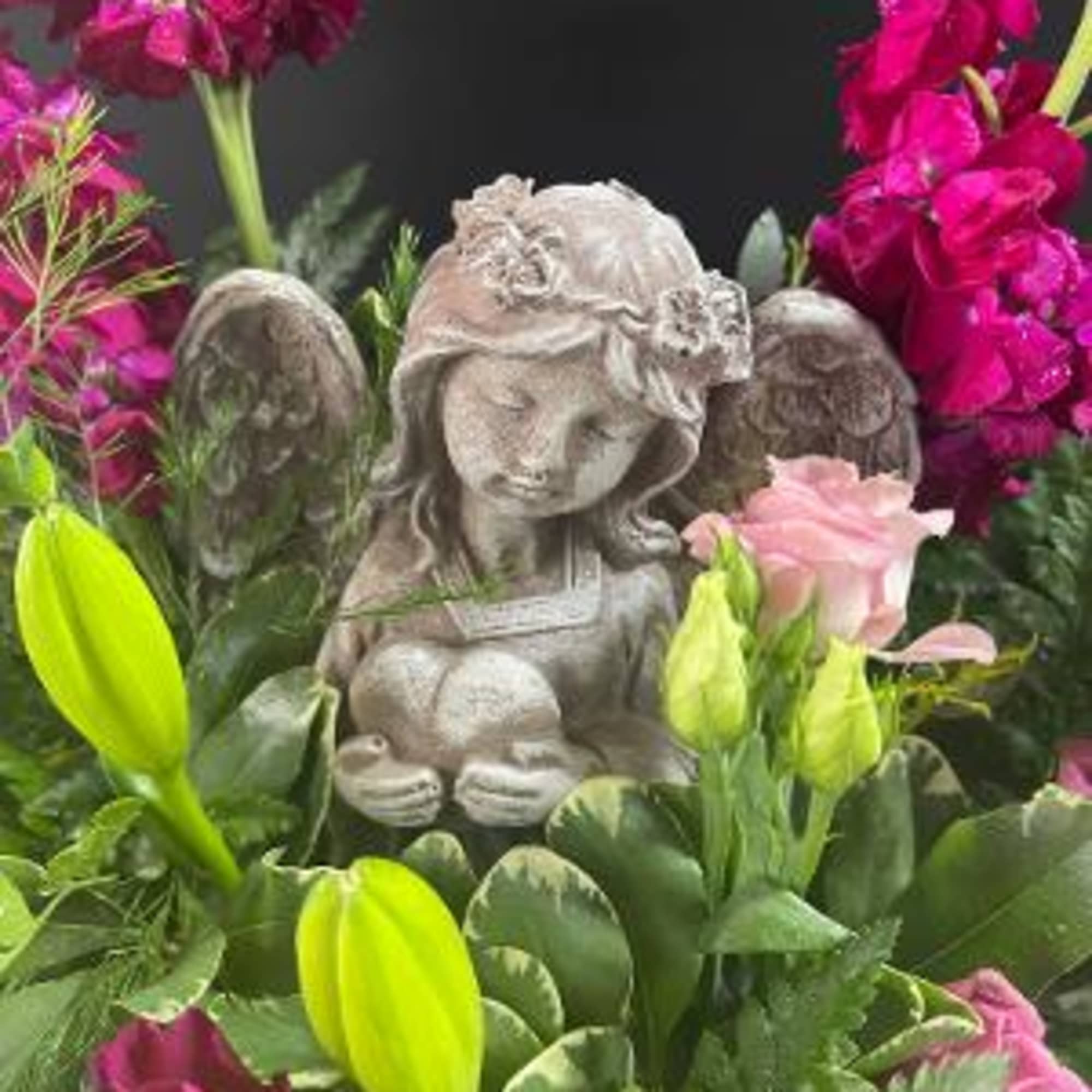 Pink flowers surround a small stone angel statue in a floral arrangement.