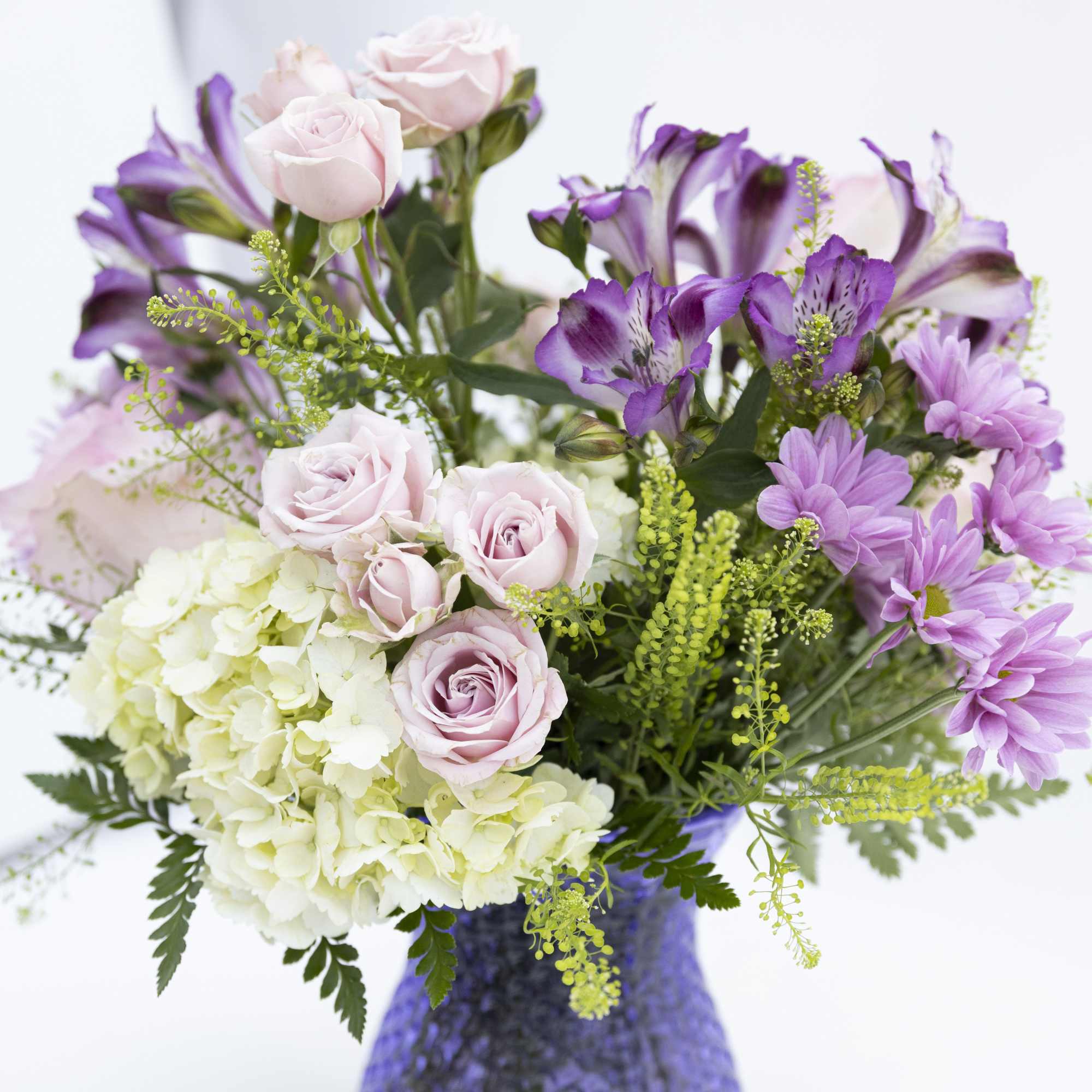 Bouquet of pale pink roses, purple alstroemeria, and white hydrangea in a purple vase