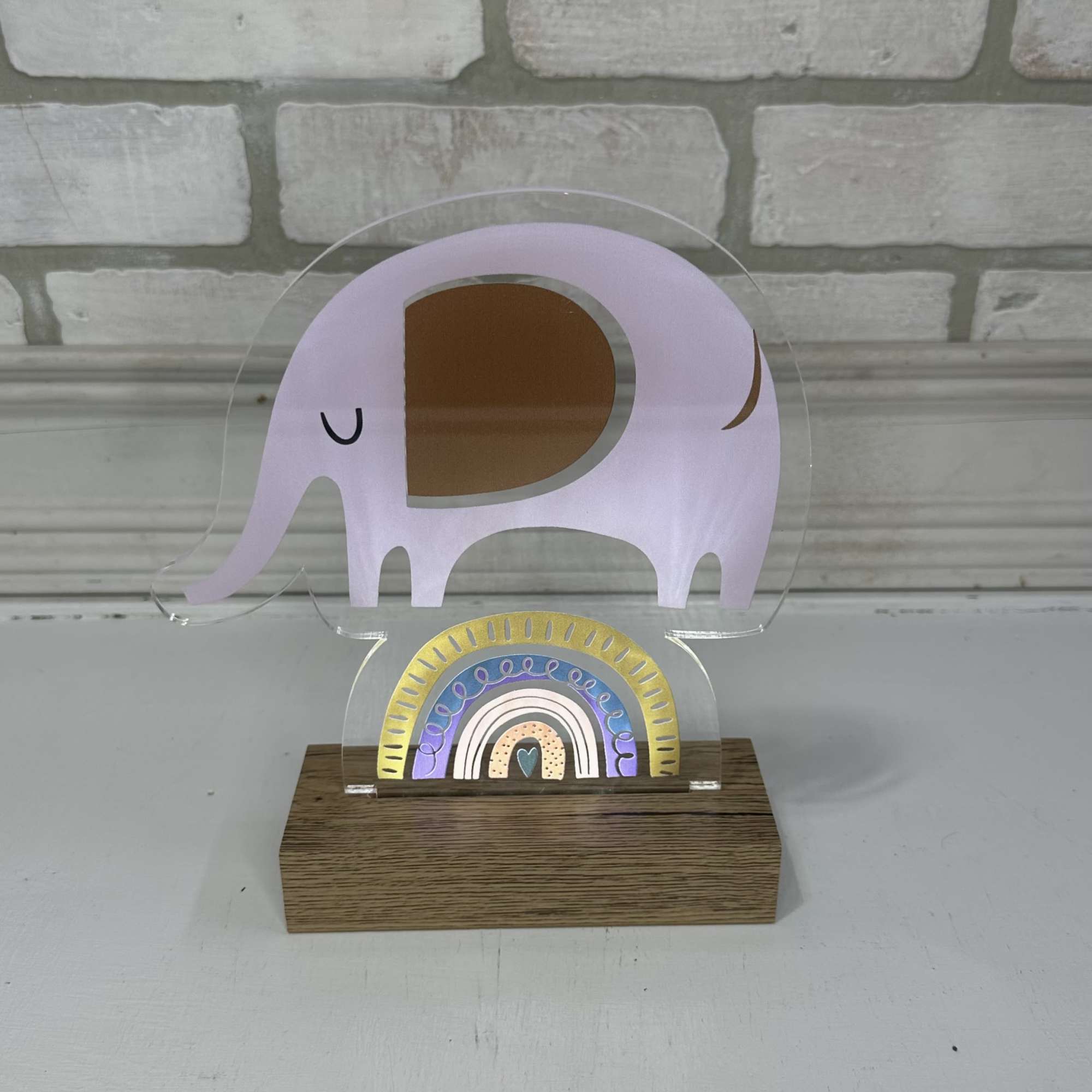A clear acrylic elephant-shaped decor piece on a wood base with a small rainbow design