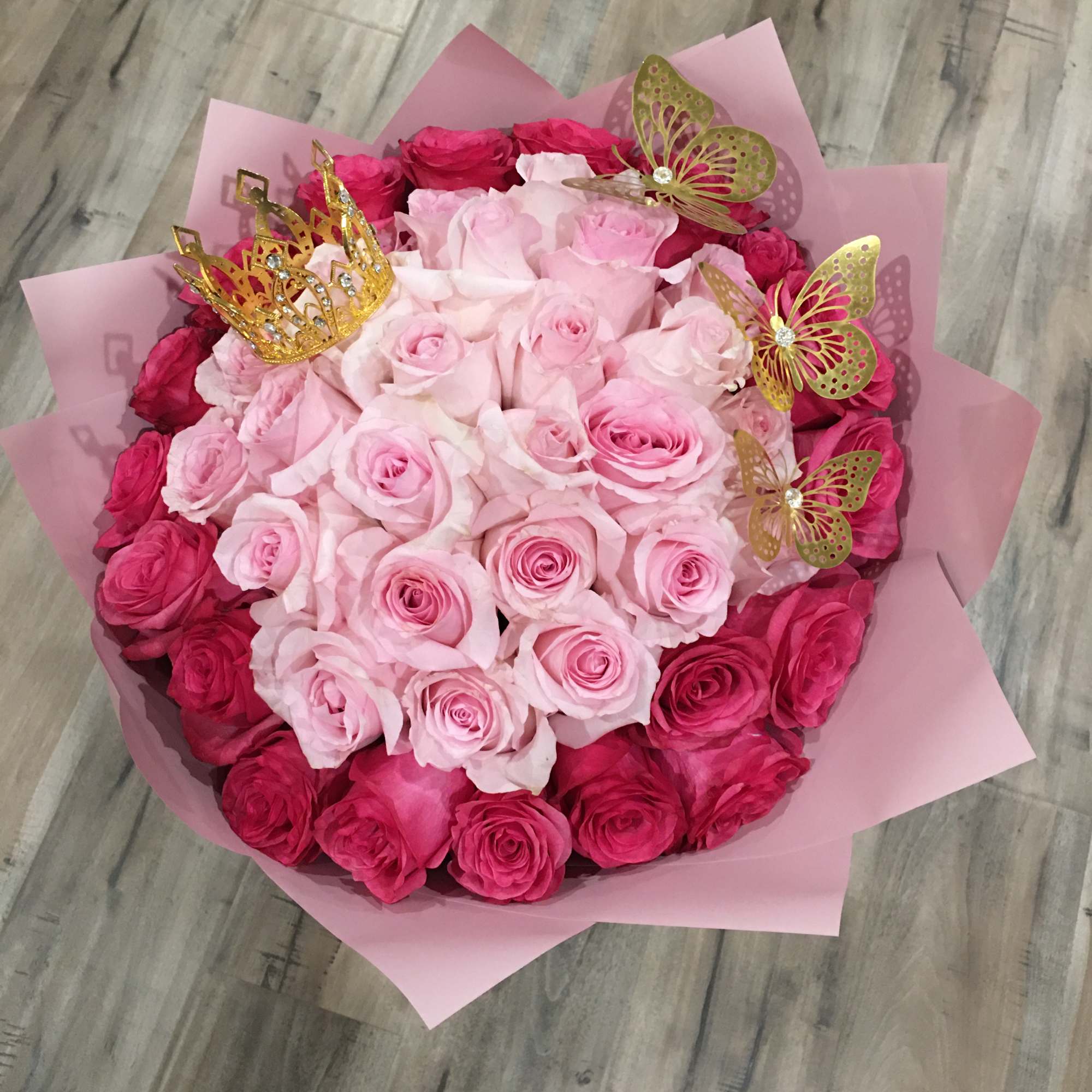 Round bouquet of pink roses with gold butterfly picks and a crown topper