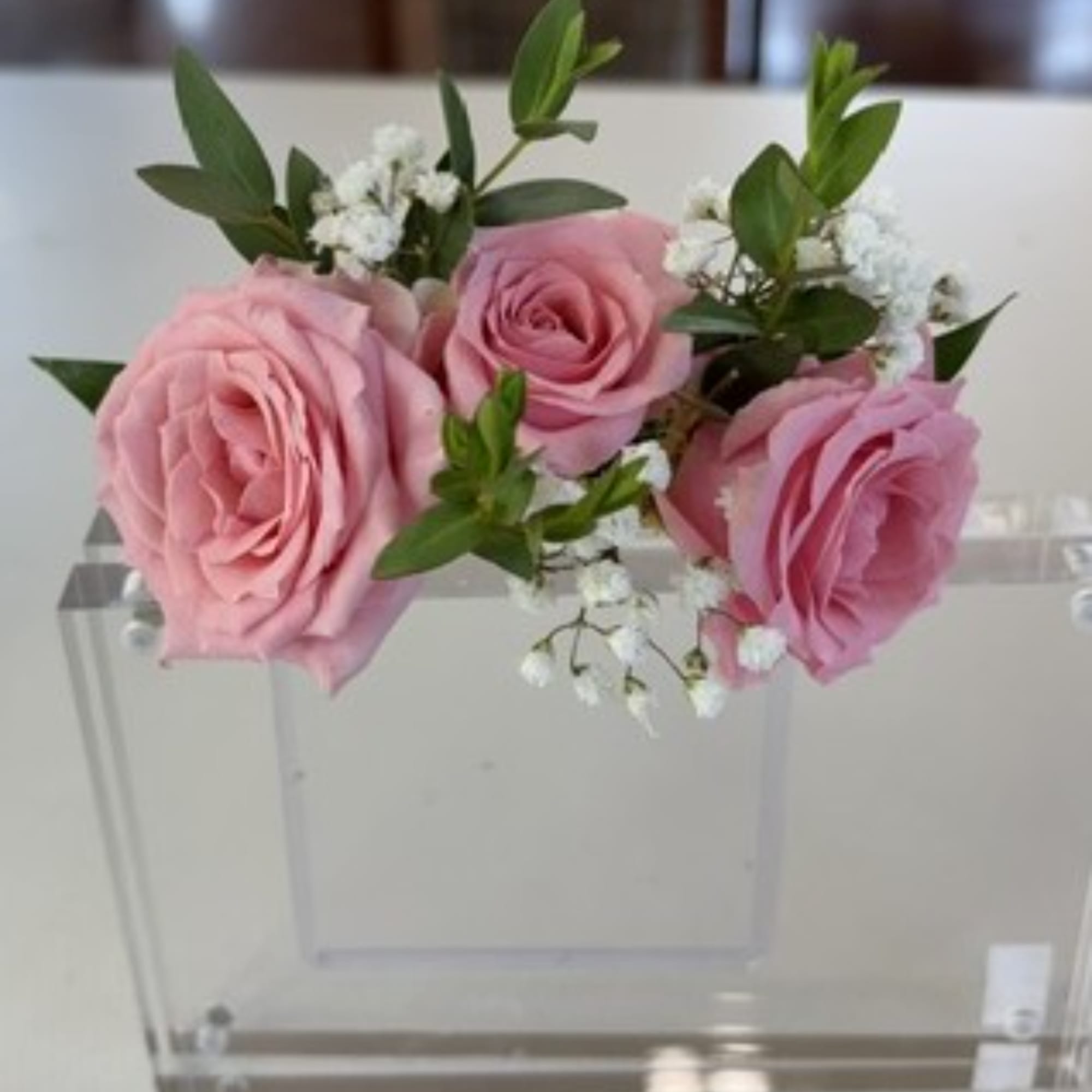 Pink roses with white filler flowers in a clear acrylic box