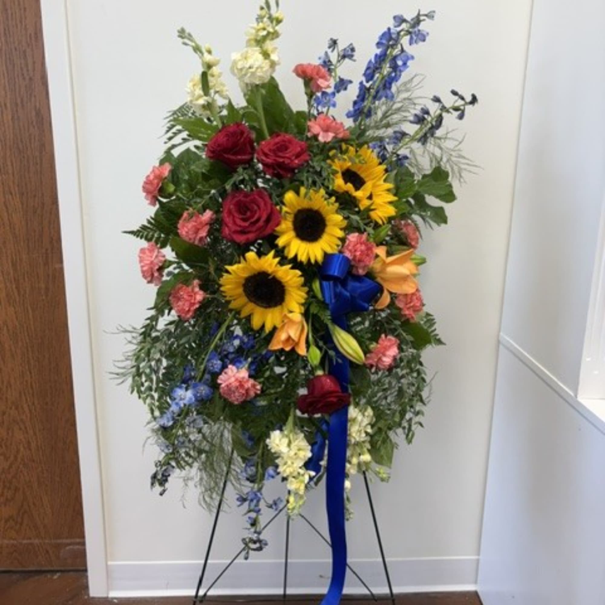 Standing floral spray with sunflowers, red roses, and blue flowers on an easel