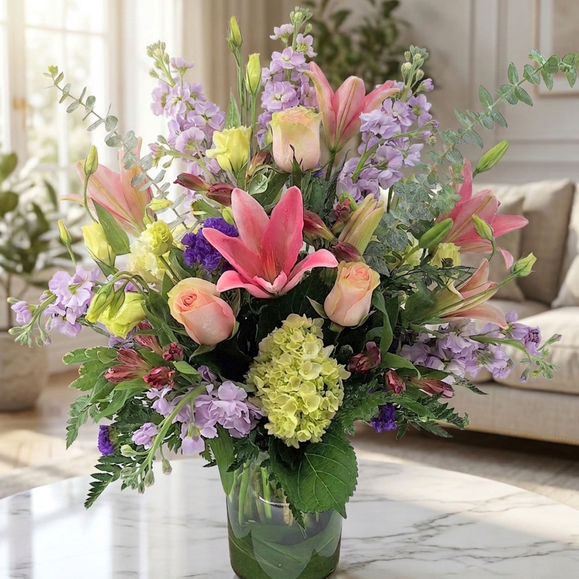 Mixed bouquet of pink lilies, roses, and lavender flowers in a glass vase