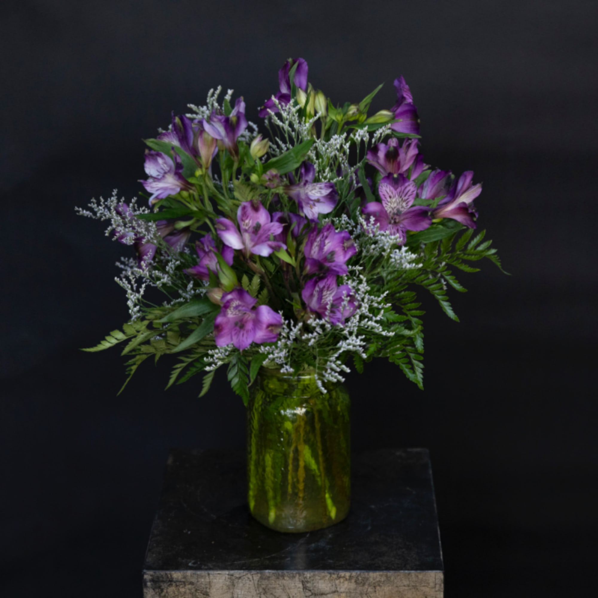 Purple alstroemeria bouquet in a green glass jar vase