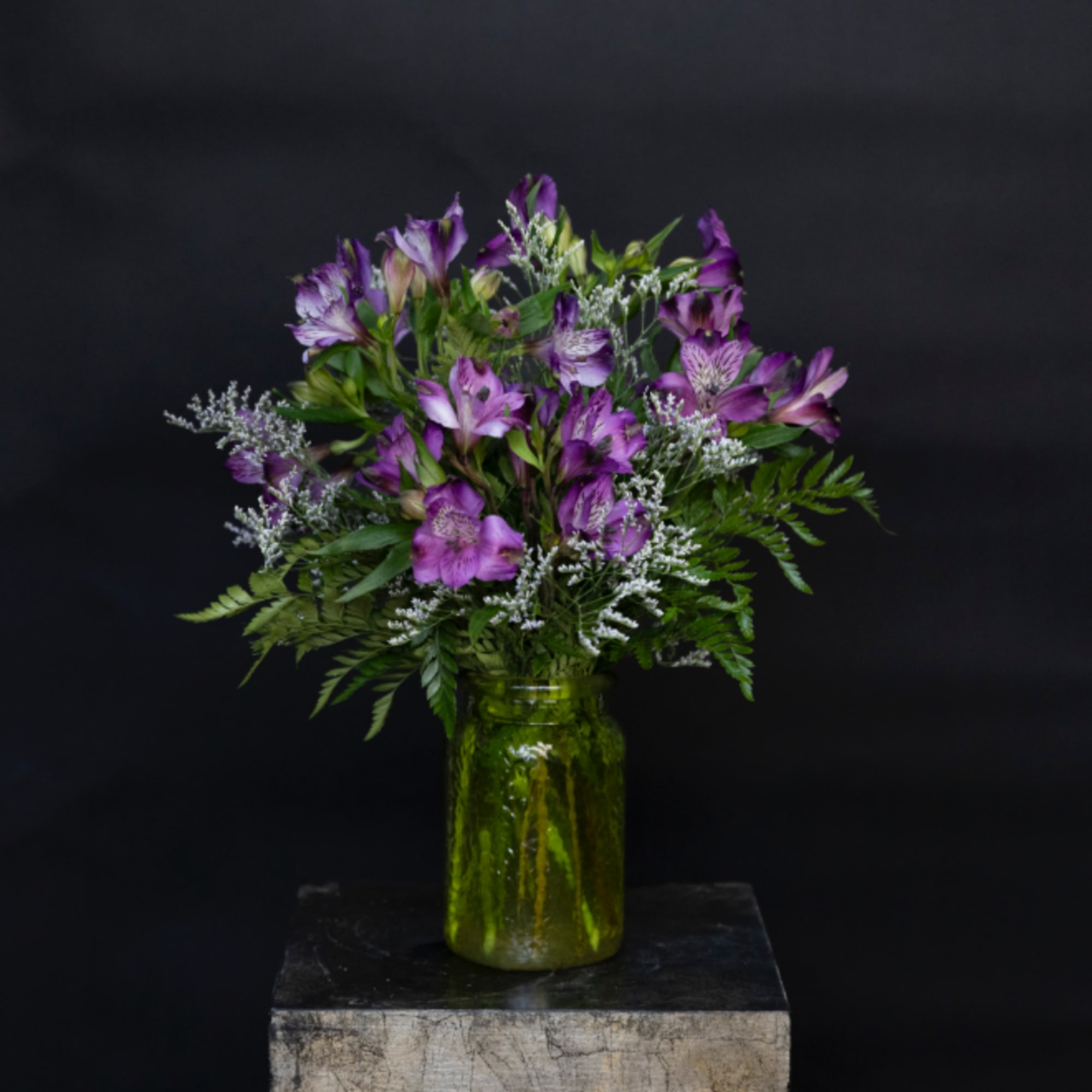 Purple alstroemeria bouquet in a green glass vase