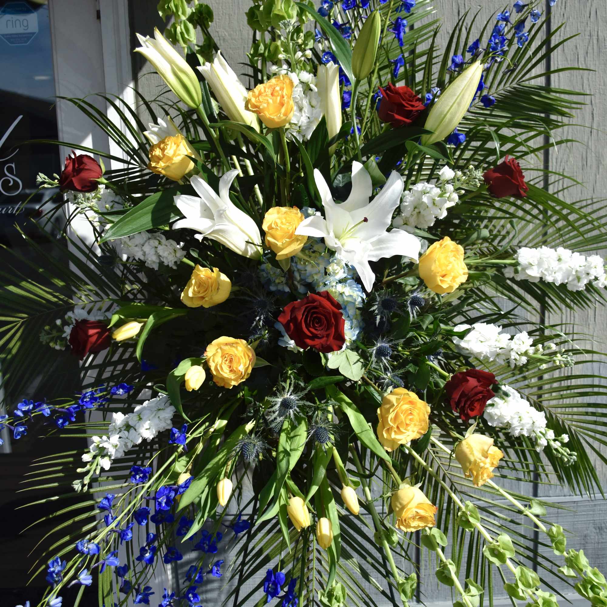 Large standing floral spray with roses, lilies, and blue flowers