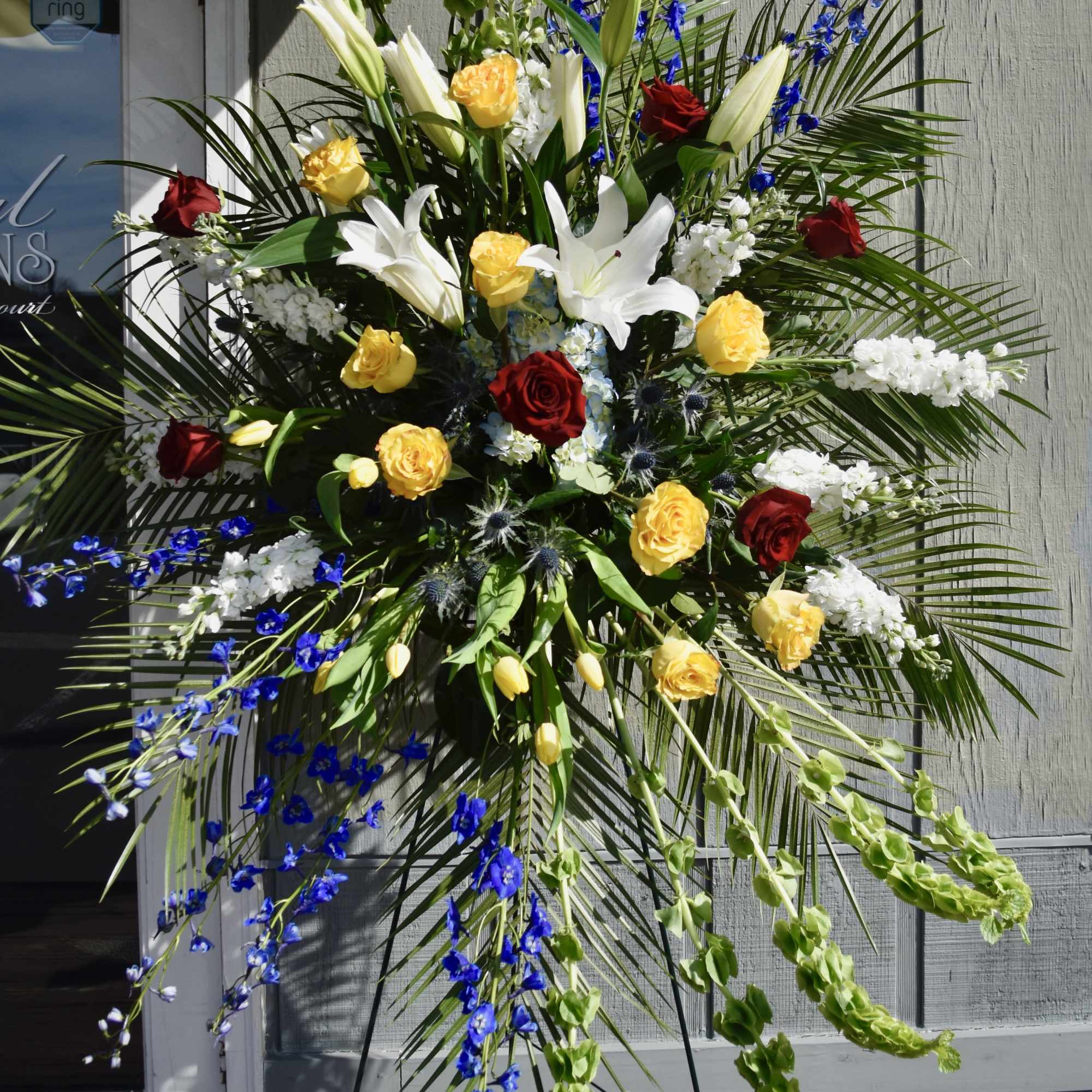 Large standing floral spray with white lilies, roses, and blue flowers