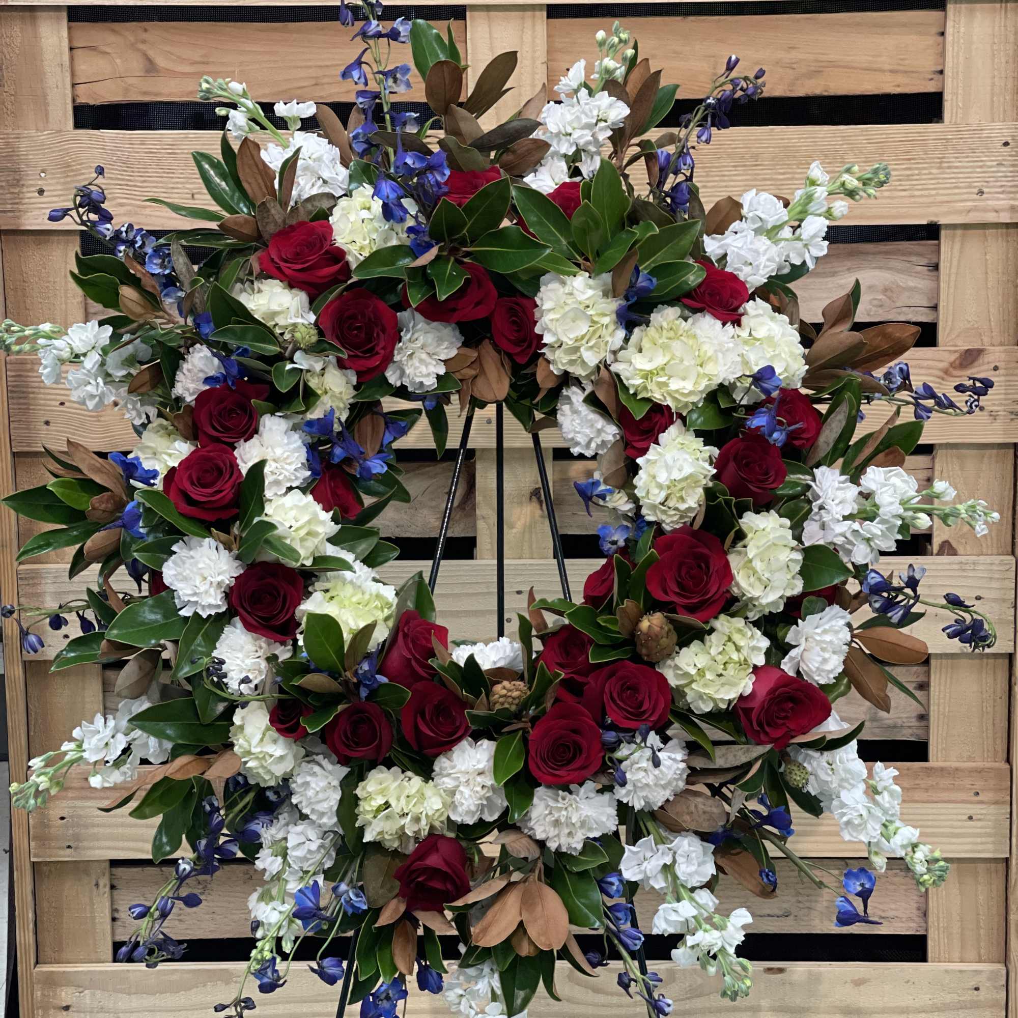 Heart-shaped floral wreath with red roses, white blooms, and blue accents