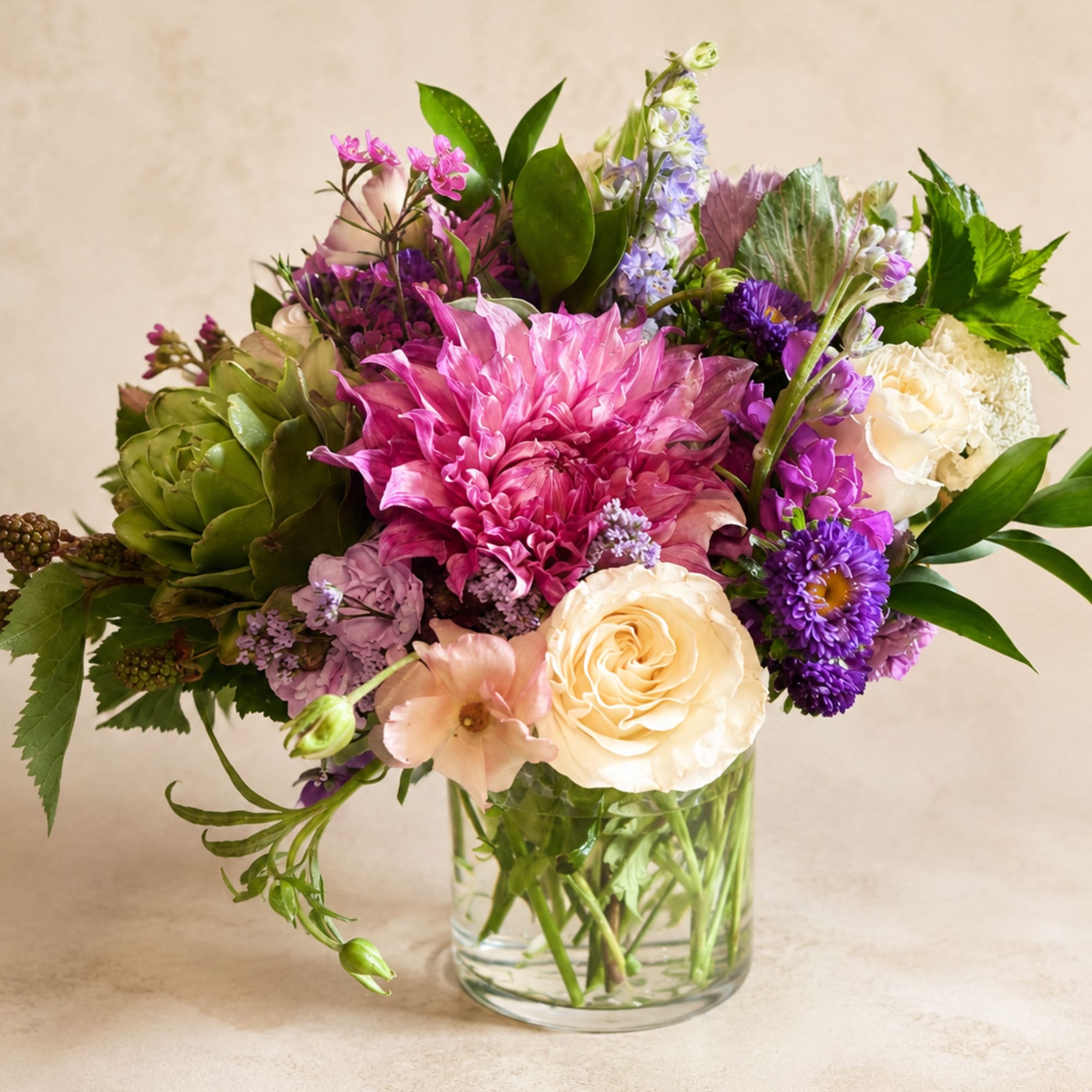 Mixed pink, purple, and white flowers arranged in a clear glass vase
