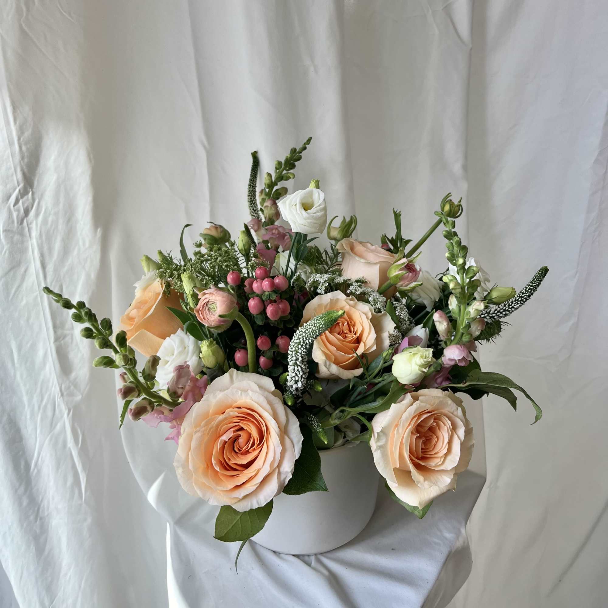 Peach and white roses arranged in a white vase with pink berries