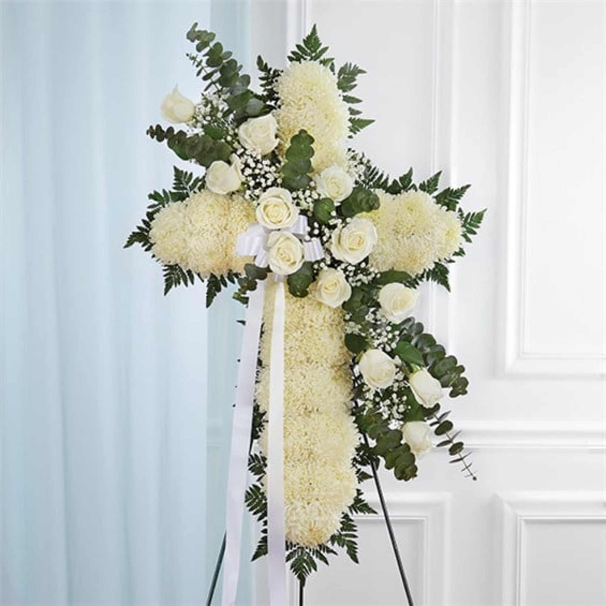 White floral cross arrangement on a stand with ribbon