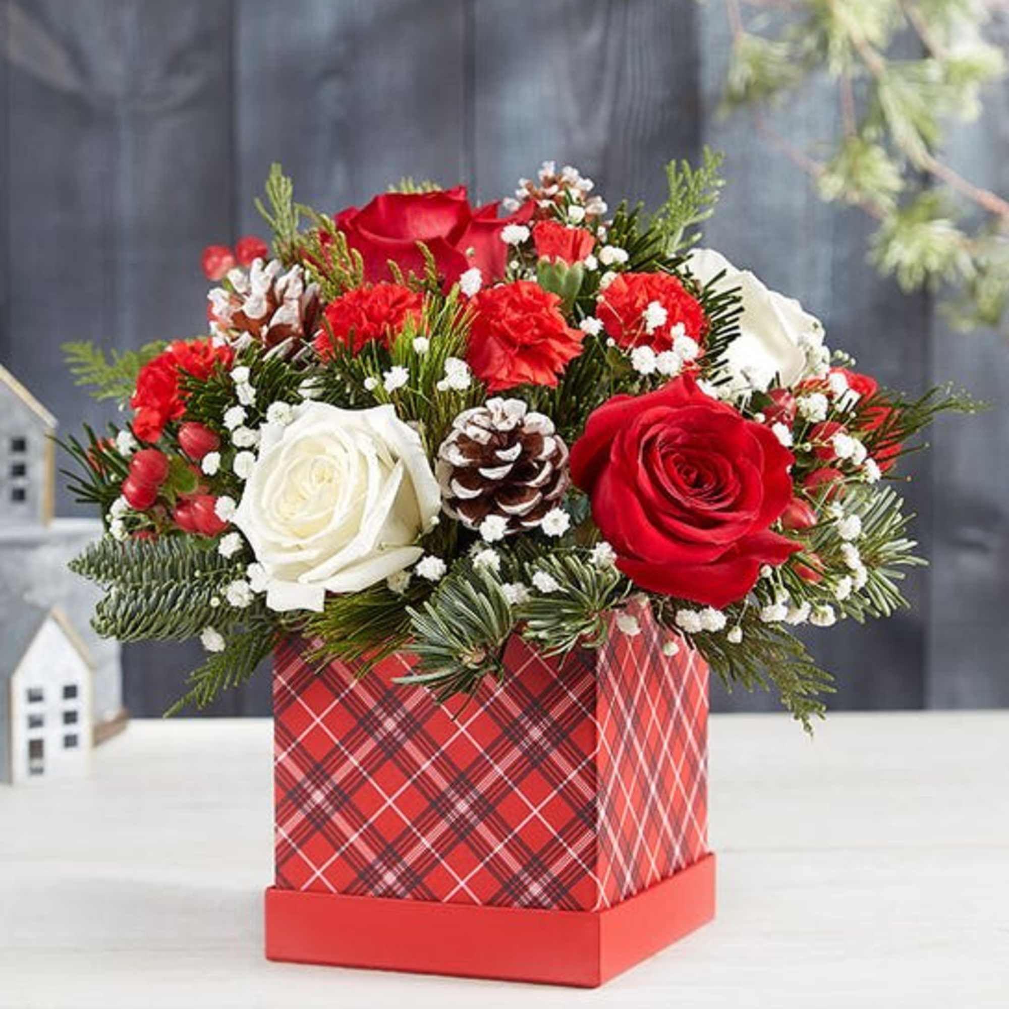 Red and white rose arrangement in a plaid gift box with pinecones