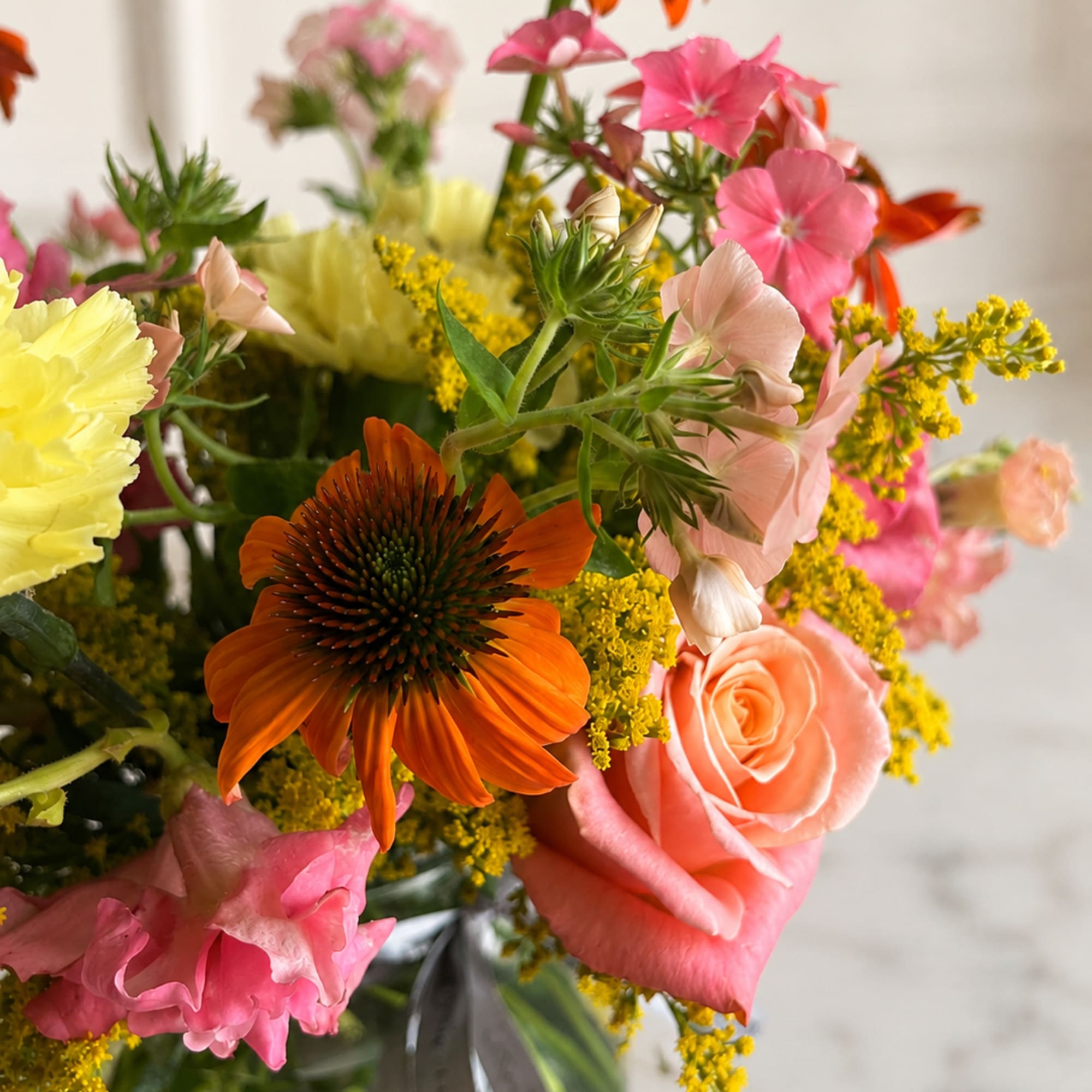 Mixed bouquet with orange coneflowers, pink roses, and yellow filler in a glass vase