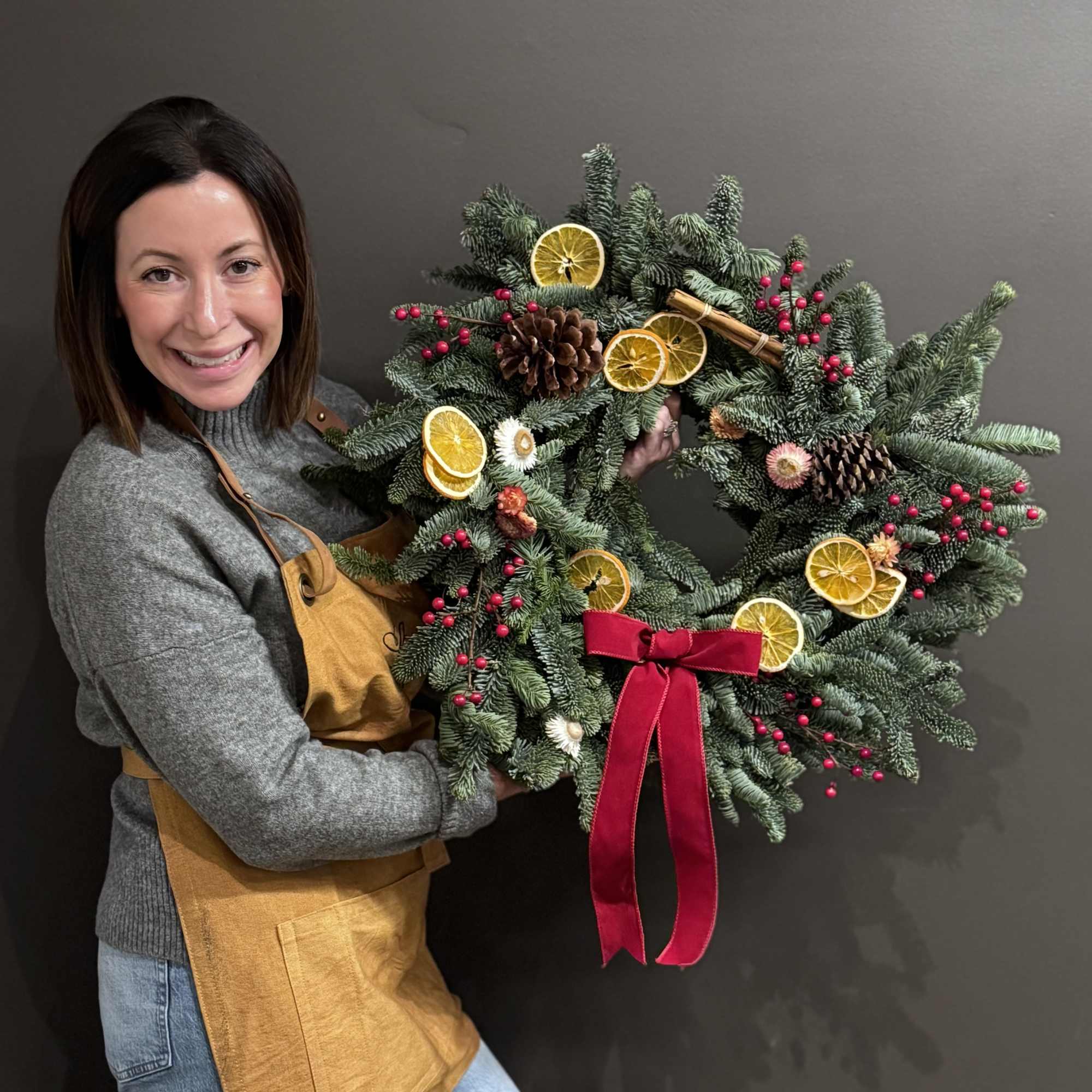 Woman holding a holiday wreath with dried orange slices, pinecones, and a red ribbon