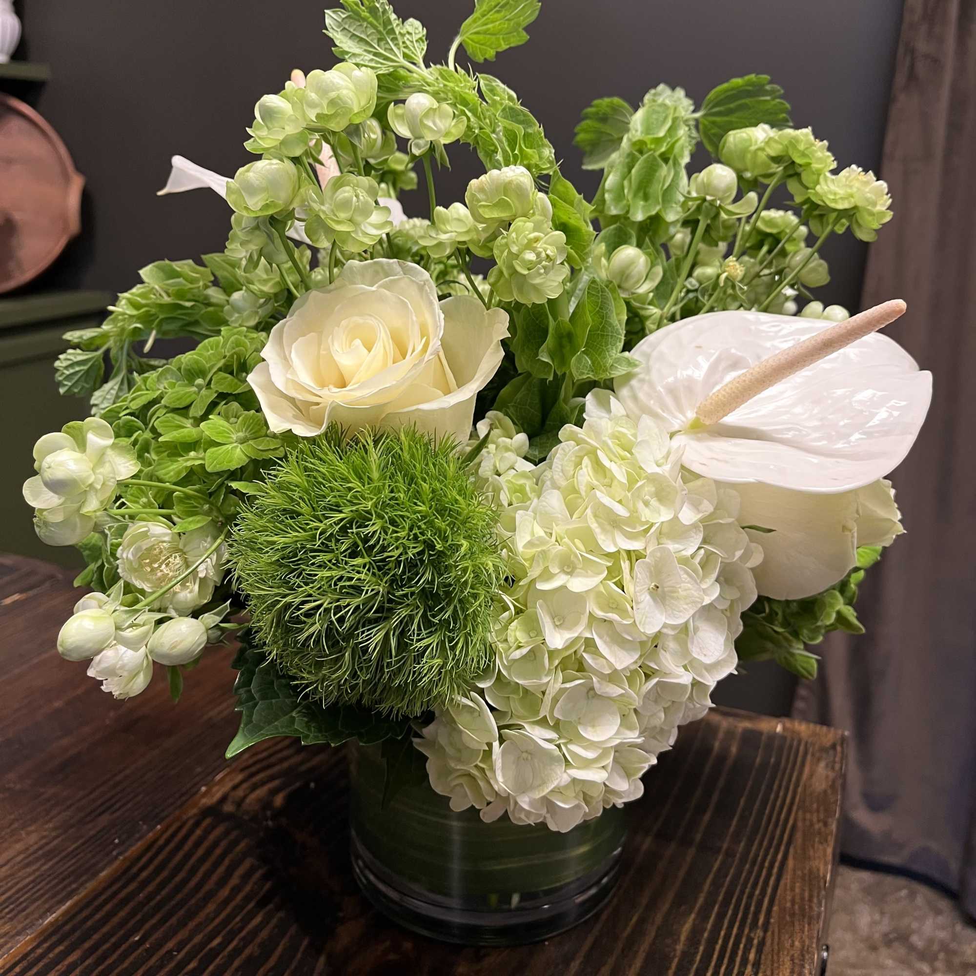 White roses and hydrangeas in a green vase with anthurium and green blooms