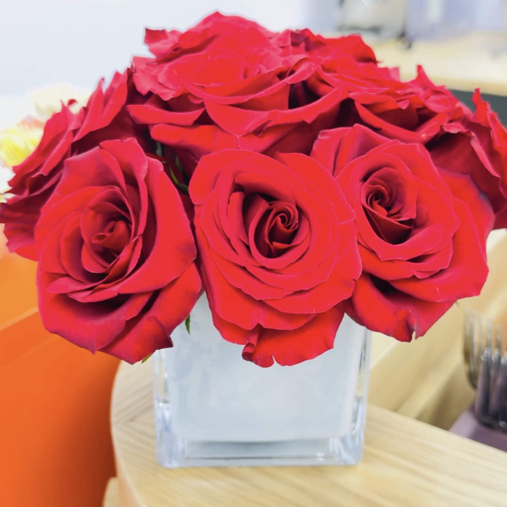 A compact cluster of vivid red roses arranged in a clear square, photo 2 of 2